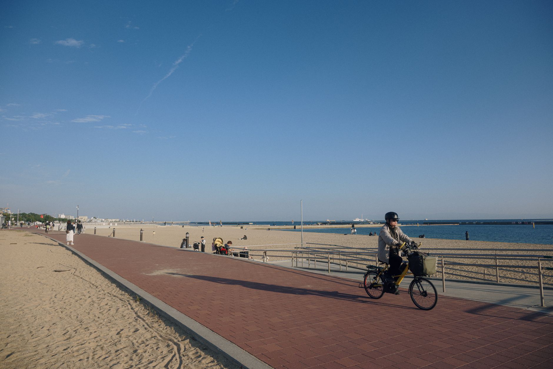 A leisurely cyclist rides by a sandy beach under a clear blue sky, ideal for summer leisure. — Trójmiasto