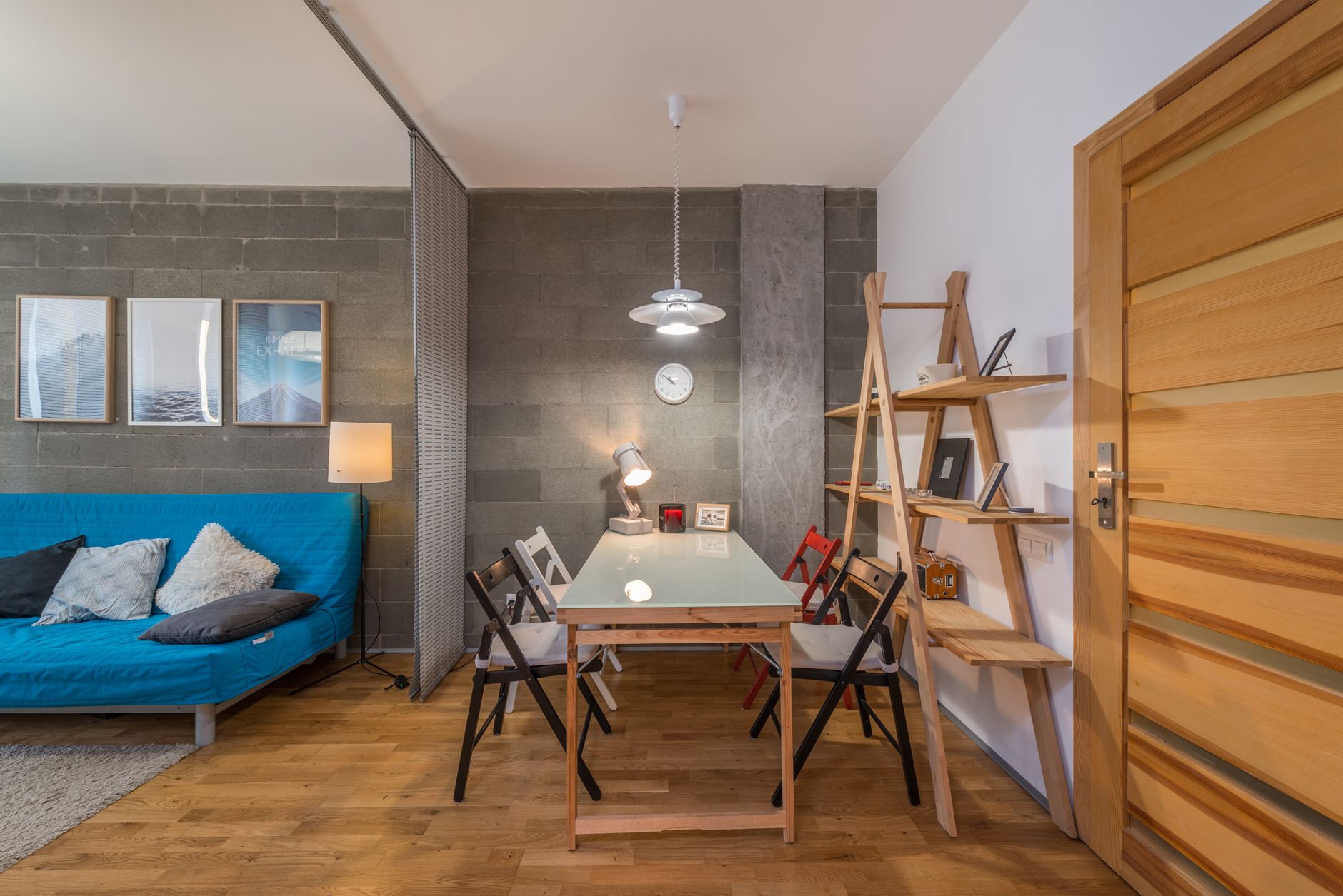 Big wooden table with colorful chairs near shelves in cozy modern living room with sofa — Trójmiasto