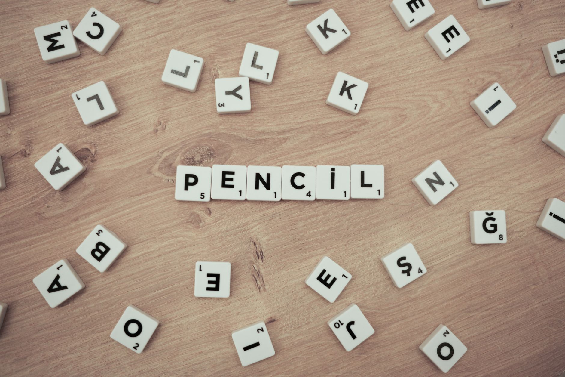 Wooden surface with scattered Scrabble tiles forming the word 'Pencil'. — Trójmiasto