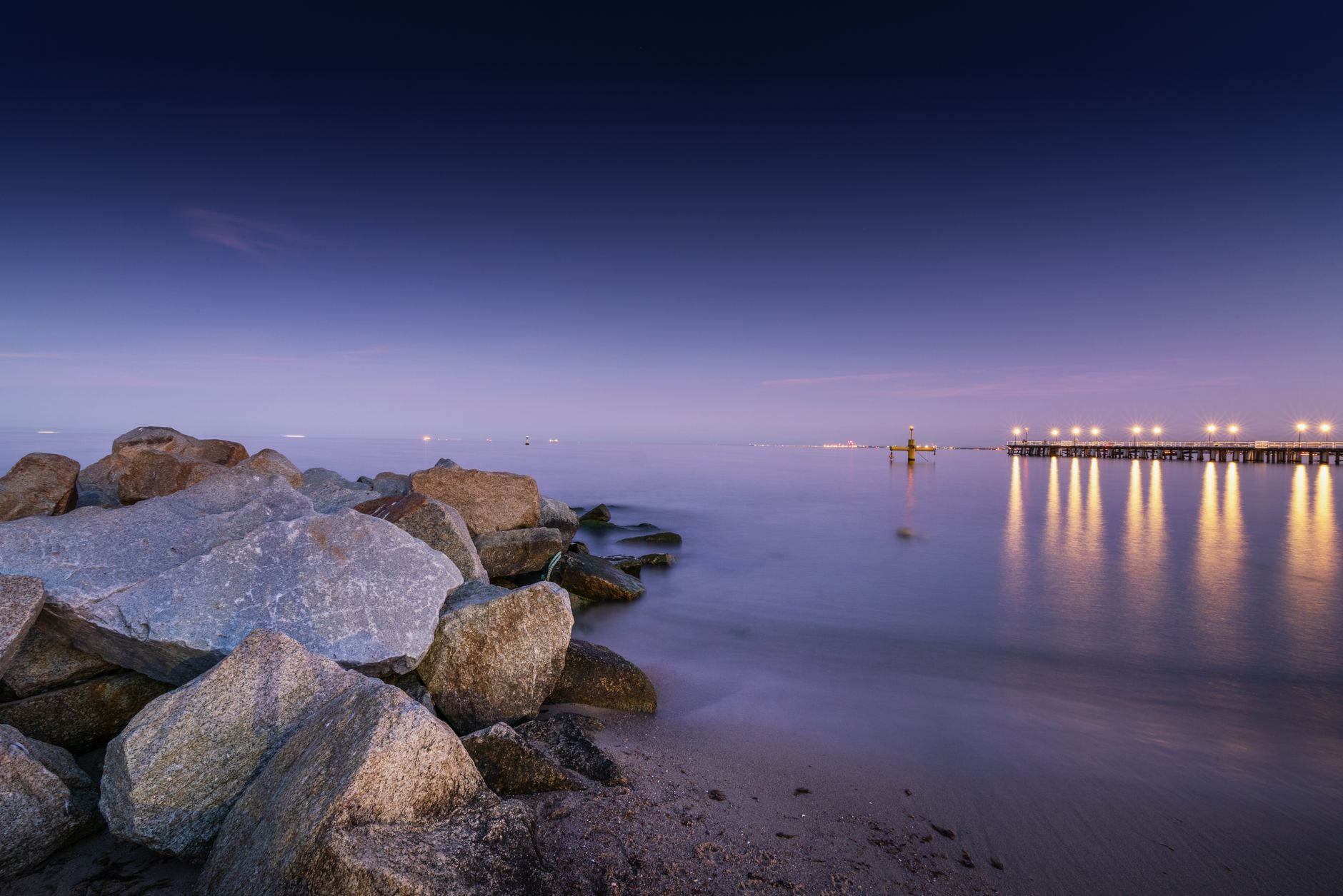 Picturesque seascape of calm sea with boulders on shore and pier on background in evening time in summer — Trójmiasto