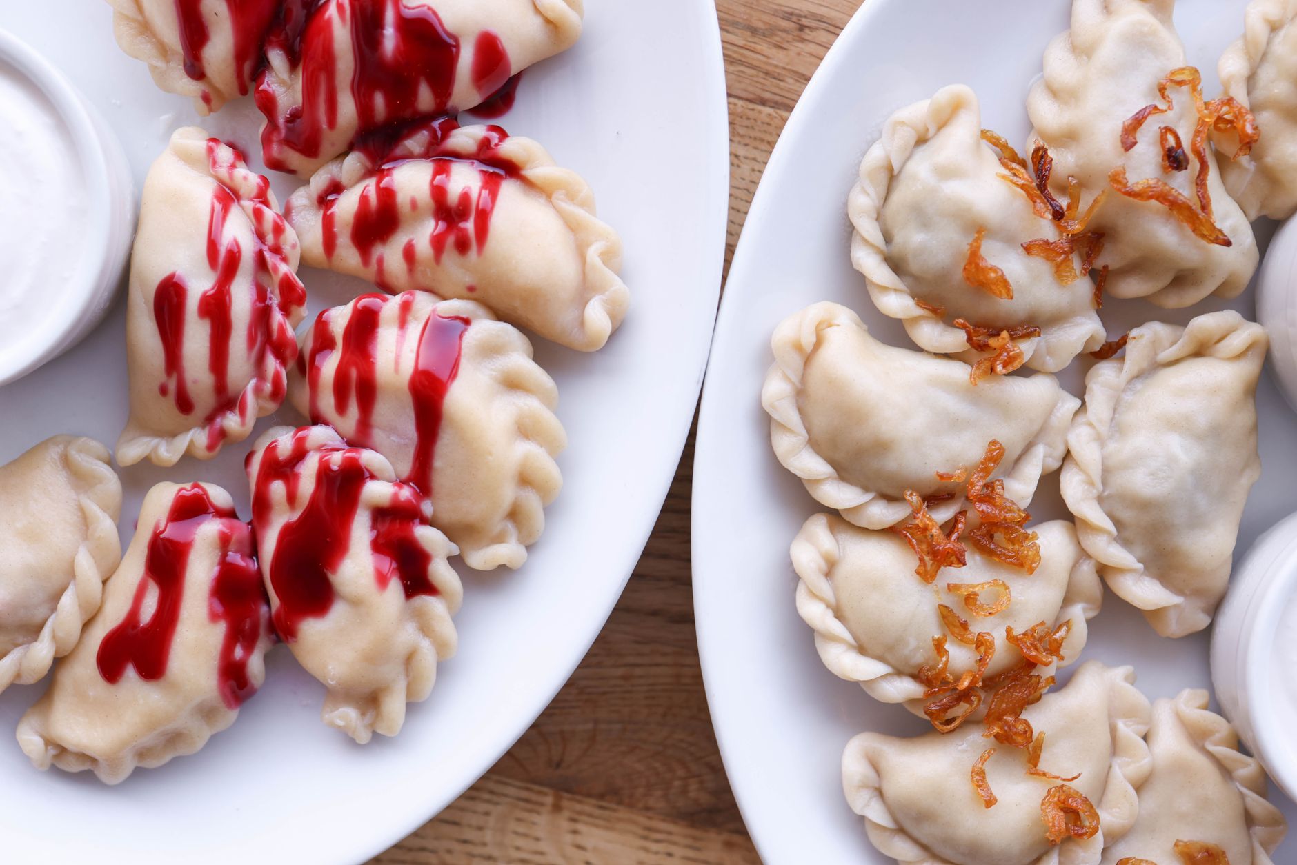 Close-up of pierogi with strawberry sauce and fried onions on white plates, perfect for culinary content. — Trójmiasto