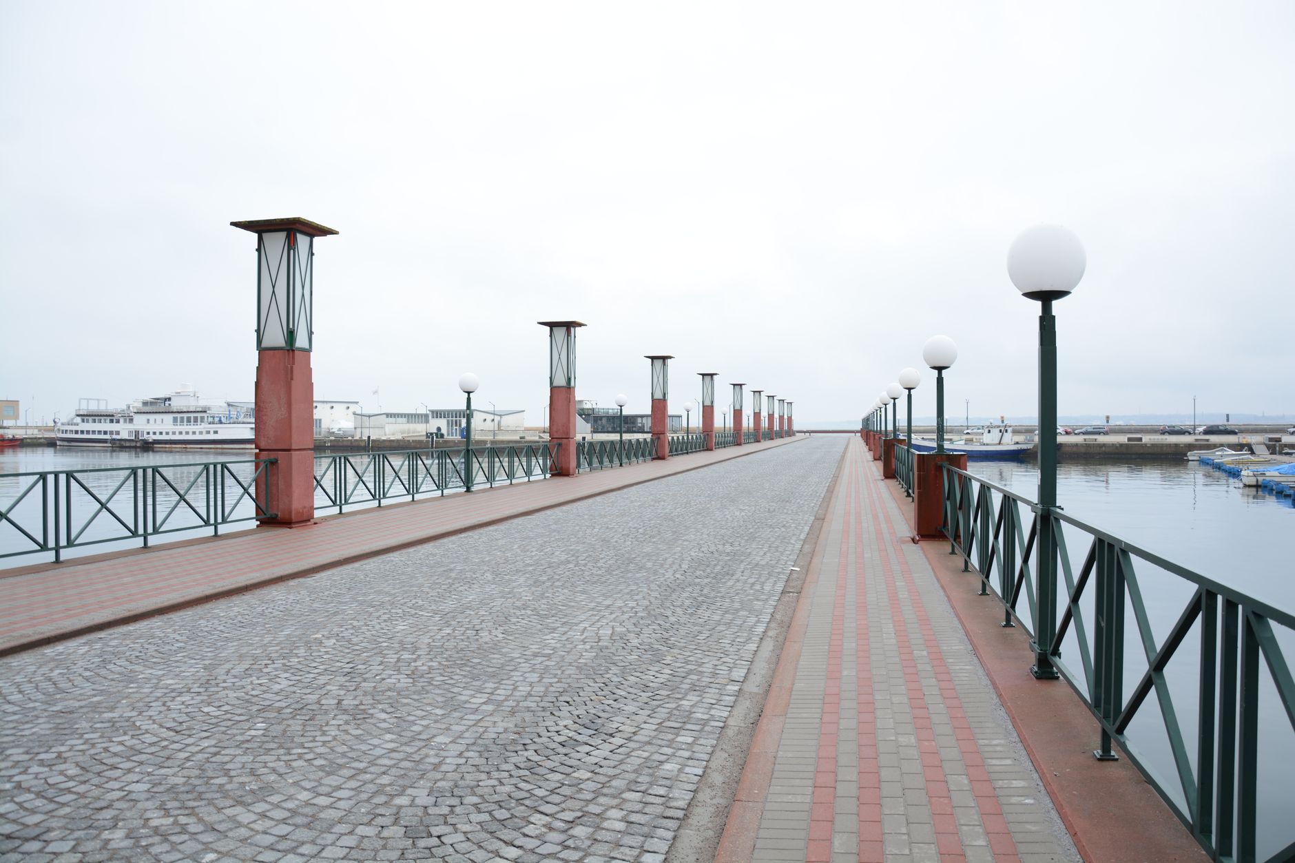 Wide view of a deserted promenade by the waterfront on an overcast day, featuring modern lamp posts and cobblestone path. — Trójmiasto