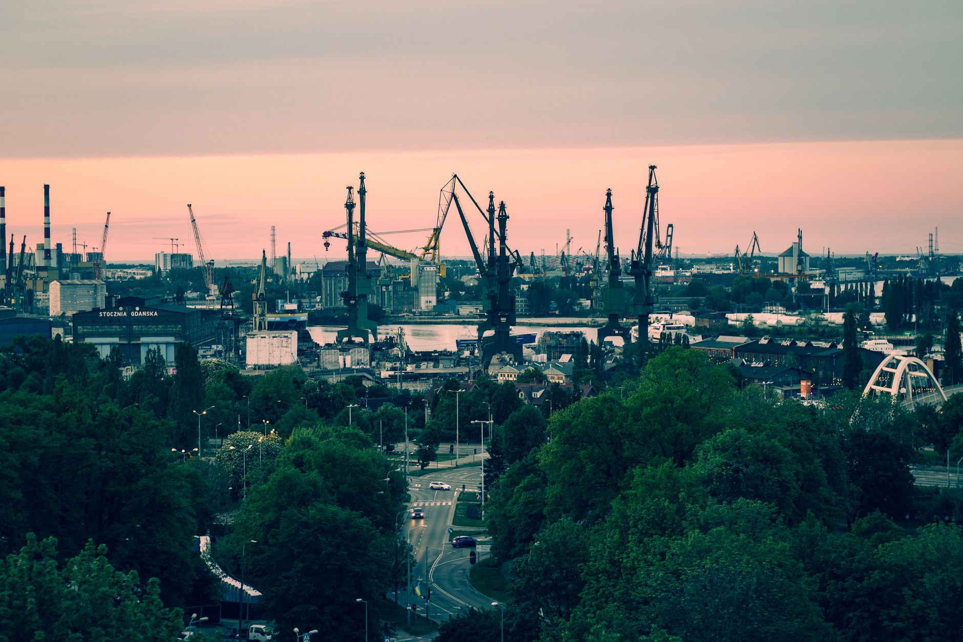 A panoramic view of the iconic Gdańsk shipyard with cranes silhouetted against a vibrant sunset sky. — Trójmiasto