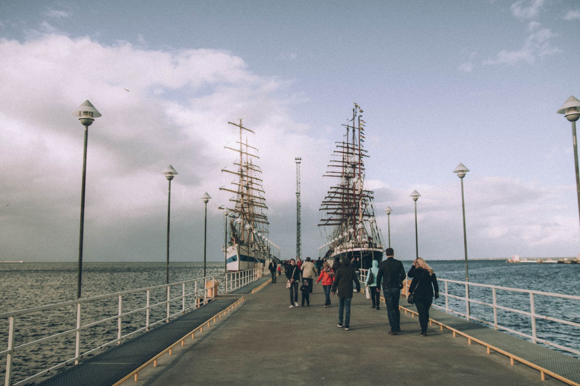 A tranquil pier scene with tall ships and tourists under a cloudy sky, ideal for travel themes. — Trójmiasto