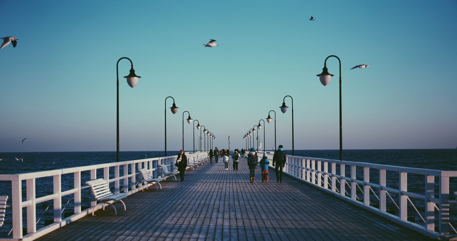 A peaceful pier in Gdynia, Poland with people strolling and seagulls flying at sunset. — Trójmiasto