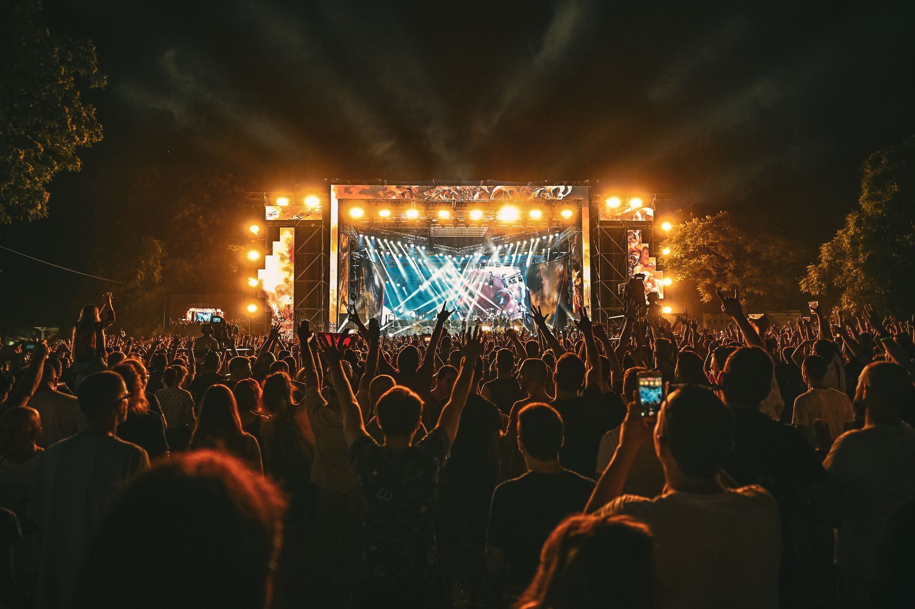 Large crowd enjoying a spectacular live outdoor concert at night with stage lighting effects. — Trójmiasto