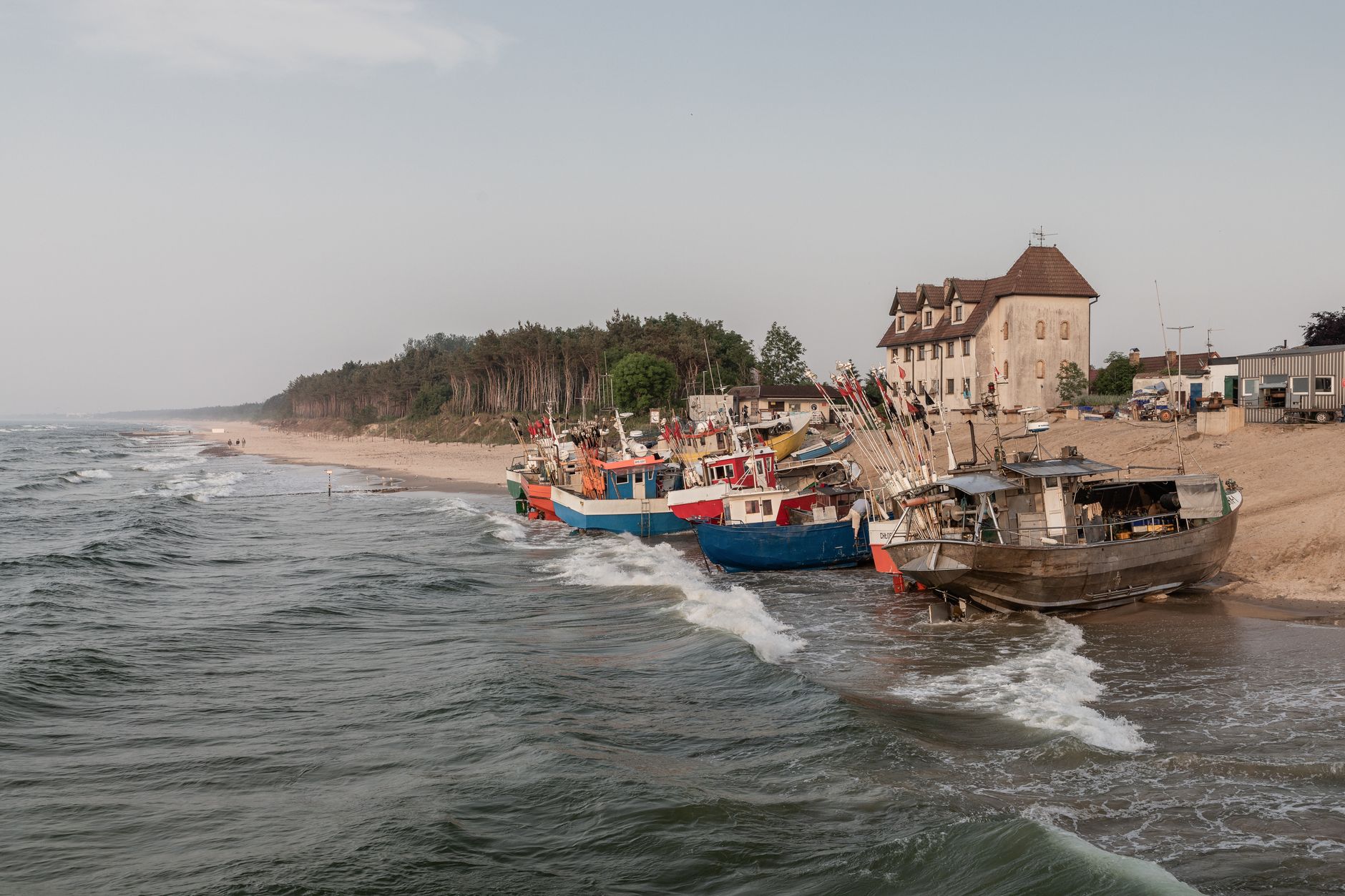 Traditional fishing boats docked along a scenic European coastline at dusk, surrounded by serene waves and rustic buildings. — Trójmiasto
