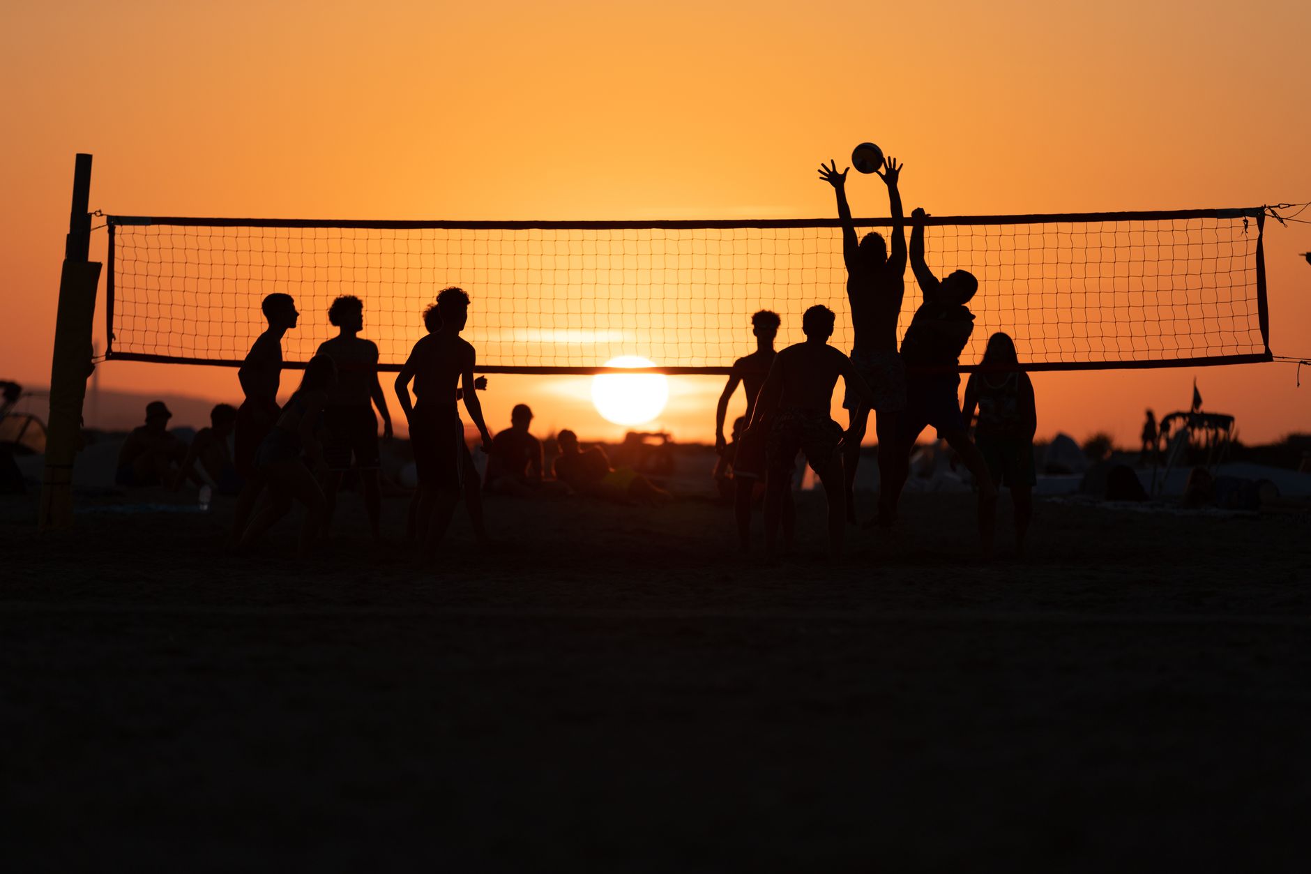 Silhouetted players enjoy a game of beach volleyball against a stunning sunset in Follonica, Italy. — Trójmiasto