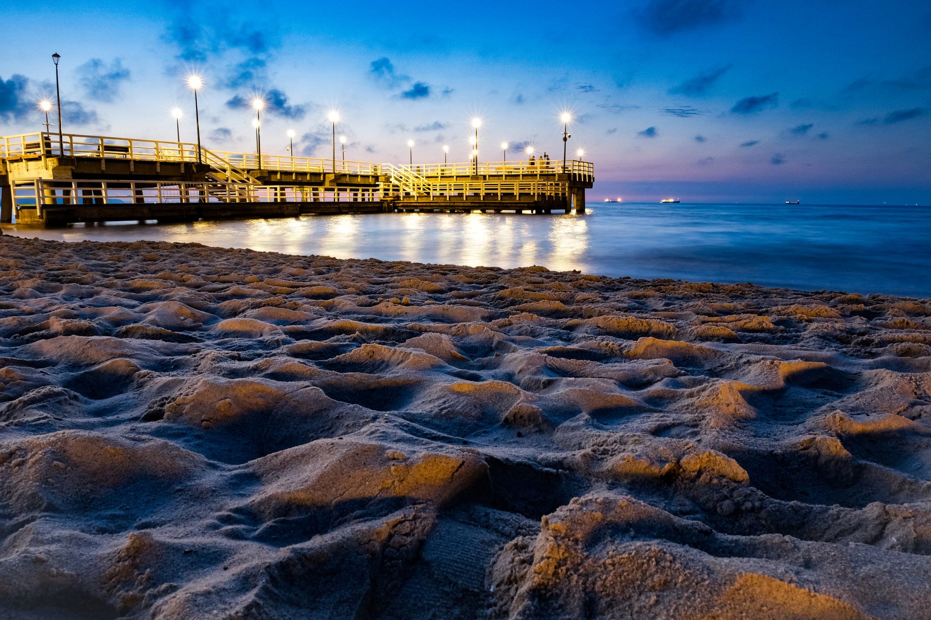 A serene evening view of the illuminated pier on the sandy beach in Gdańsk, Poland. — Trójmiasto