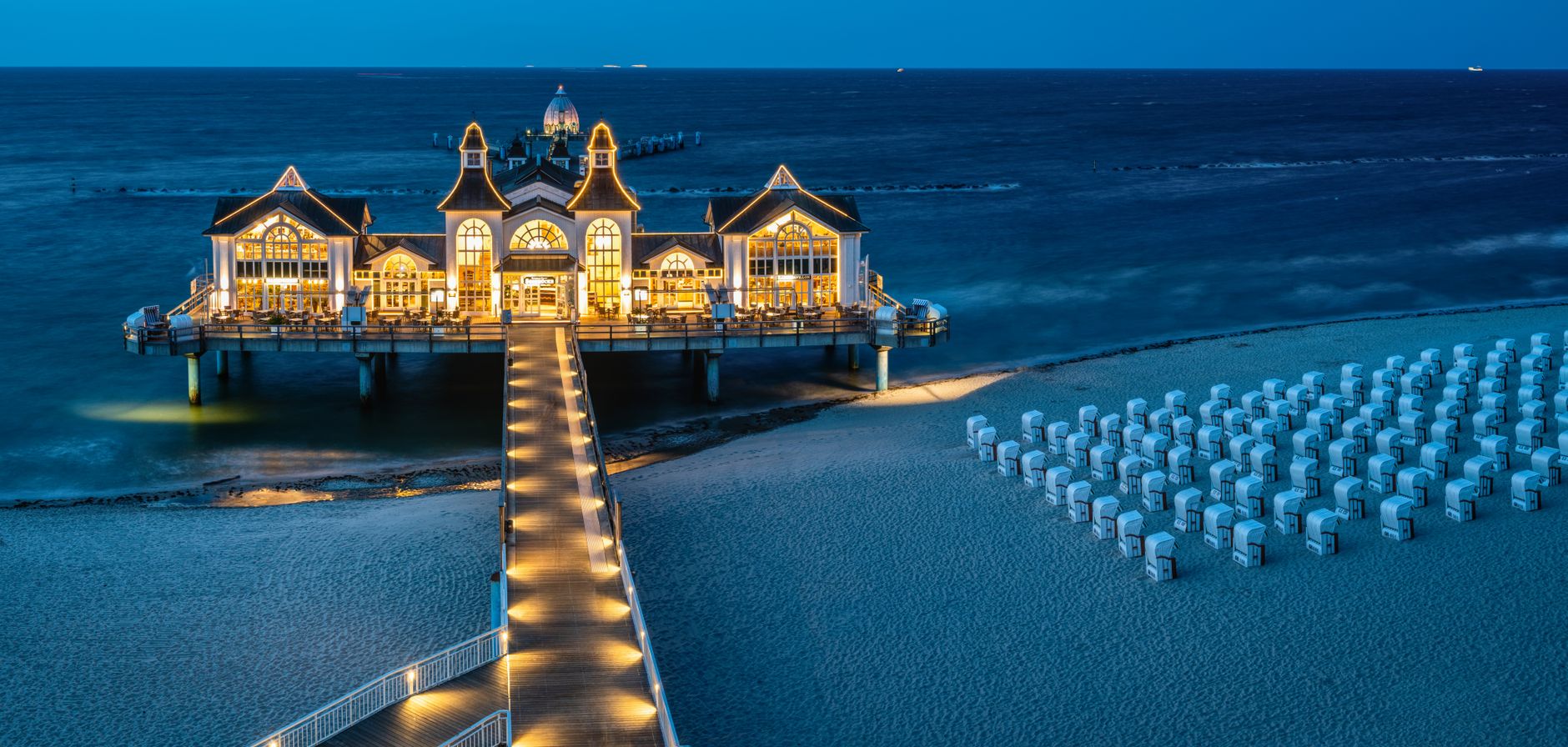A captivating view of a well-lit pier at twilight over a sandy beach by the ocean. — Trójmiasto