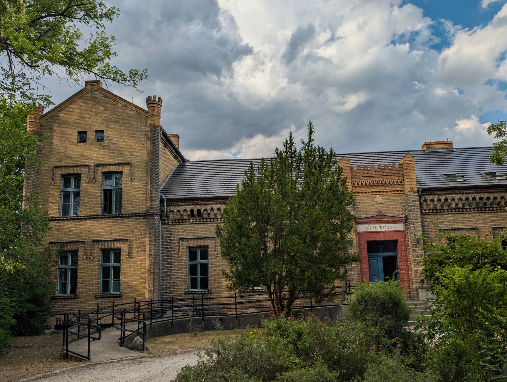 A historic brick building surrounded by lush greenery in Brandenburg, Germany, under a dramatic cloudy sky. — Trójmiasto