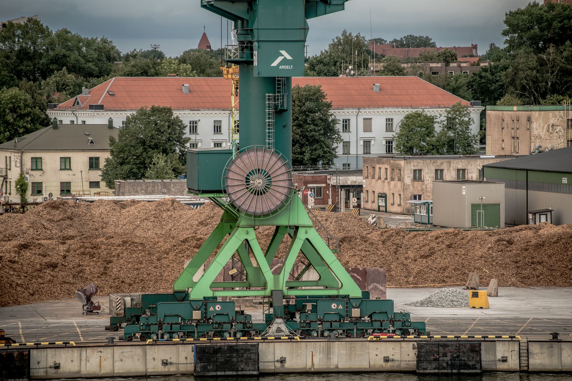 A large green industrial crane at Klaipėda Harbor, Lithuania, amidst a backdrop of buildings and trees. — Trójmiasto