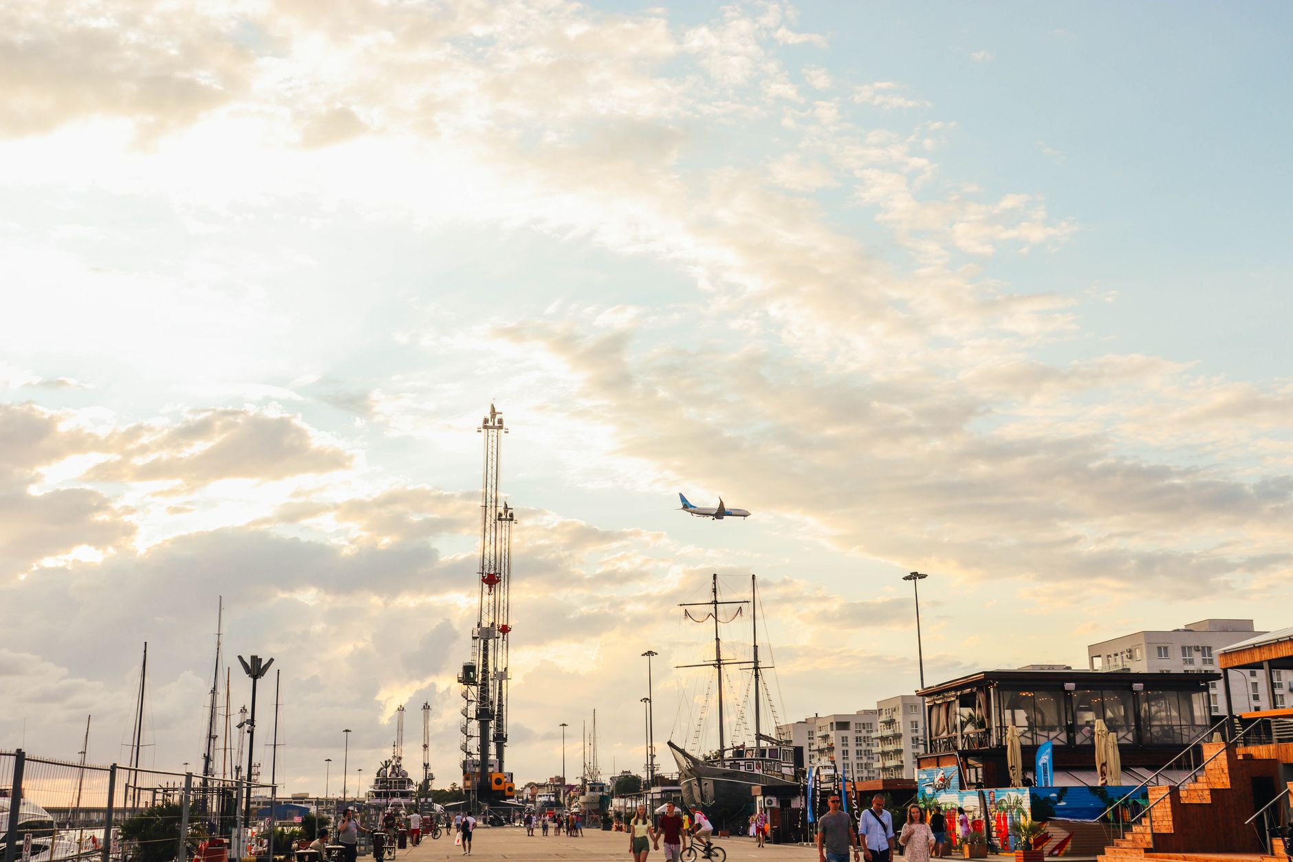 People enjoy a seaside walk in Adler, Russia, under a cloudy sky with a plane soaring above. — Trójmiasto