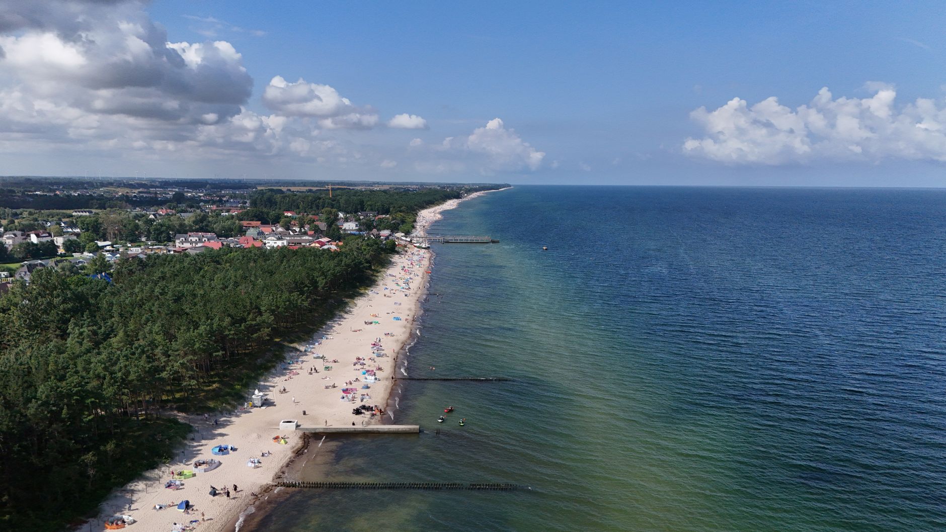 A breathtaking aerial shot of a sandy beach, vibrant ocean, and coastal town under a clear blue sky. — Trójmiasto