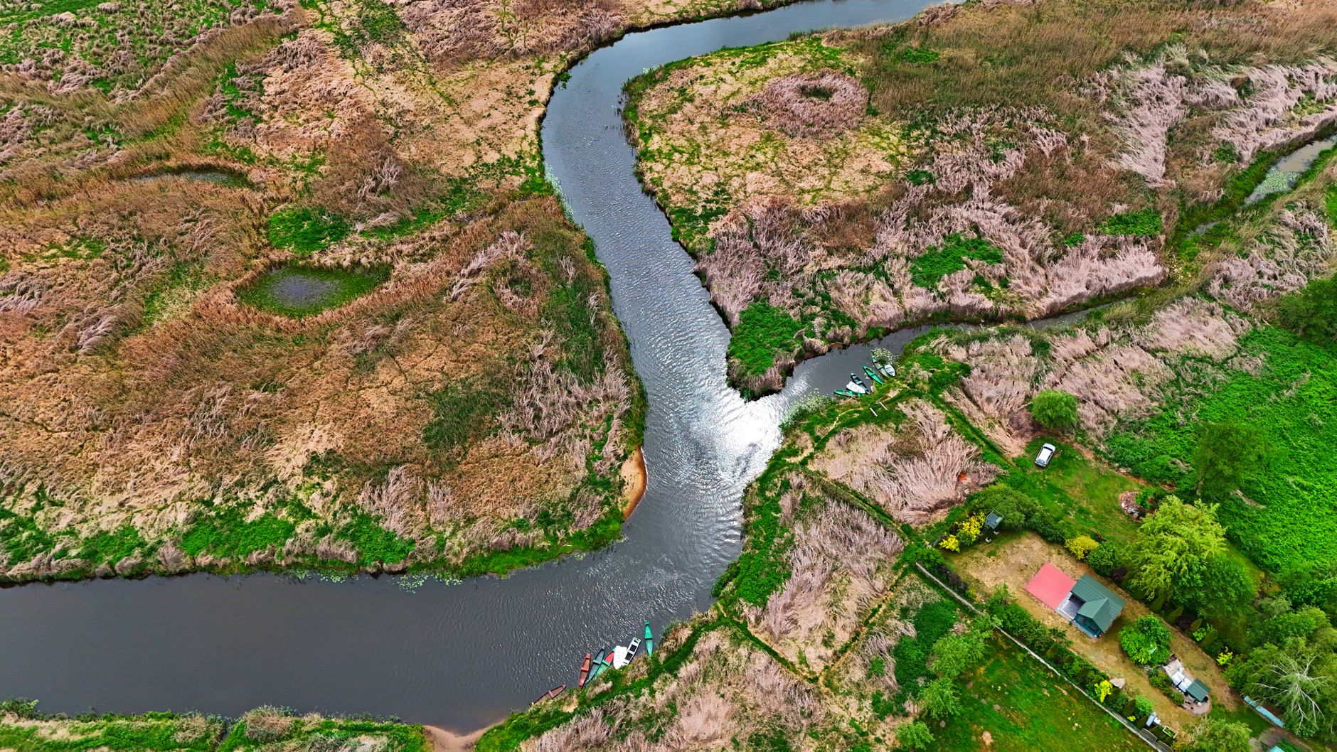 Aerial shot of a winding river through lush greenery and fields in Podlaskie Voivodeship, Poland. — Trójmiasto