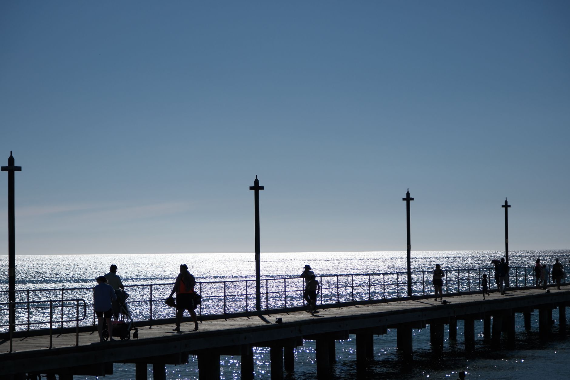 Silhouetted people walking on a pier under a bright sunset sky by the ocean, creating a serene and peaceful scene. — Trójmiasto