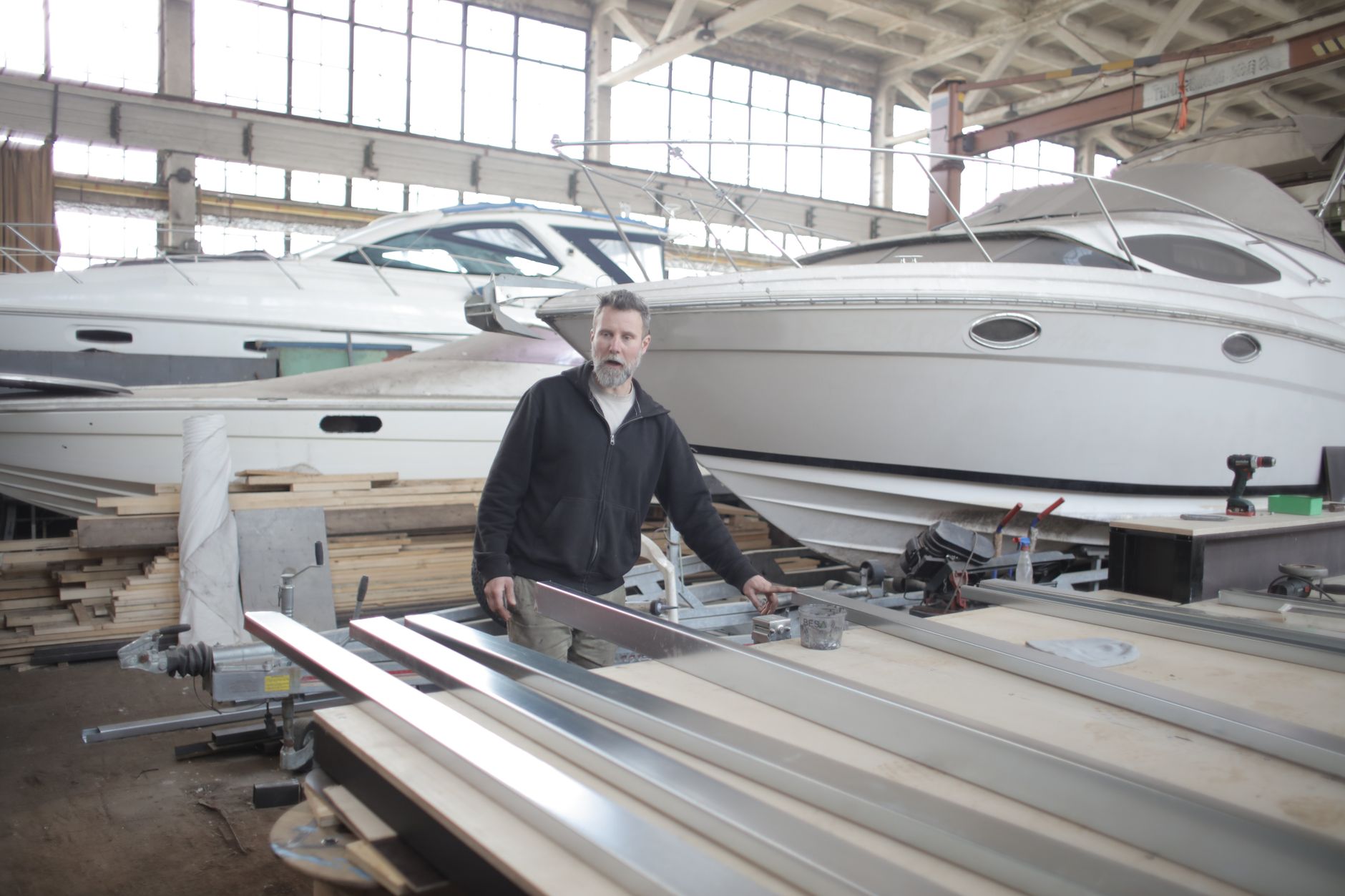 Serious brutal male mechanic wearing casual clothes standing near metal details in spacious hangar with yachts — Trójmiasto
