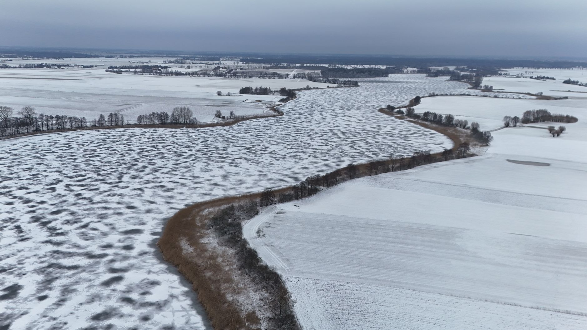 Stunning aerial photograph showcasing snow-covered fields and river in Poland during winter, emphasizing nature's serene beauty. — Trójmiasto