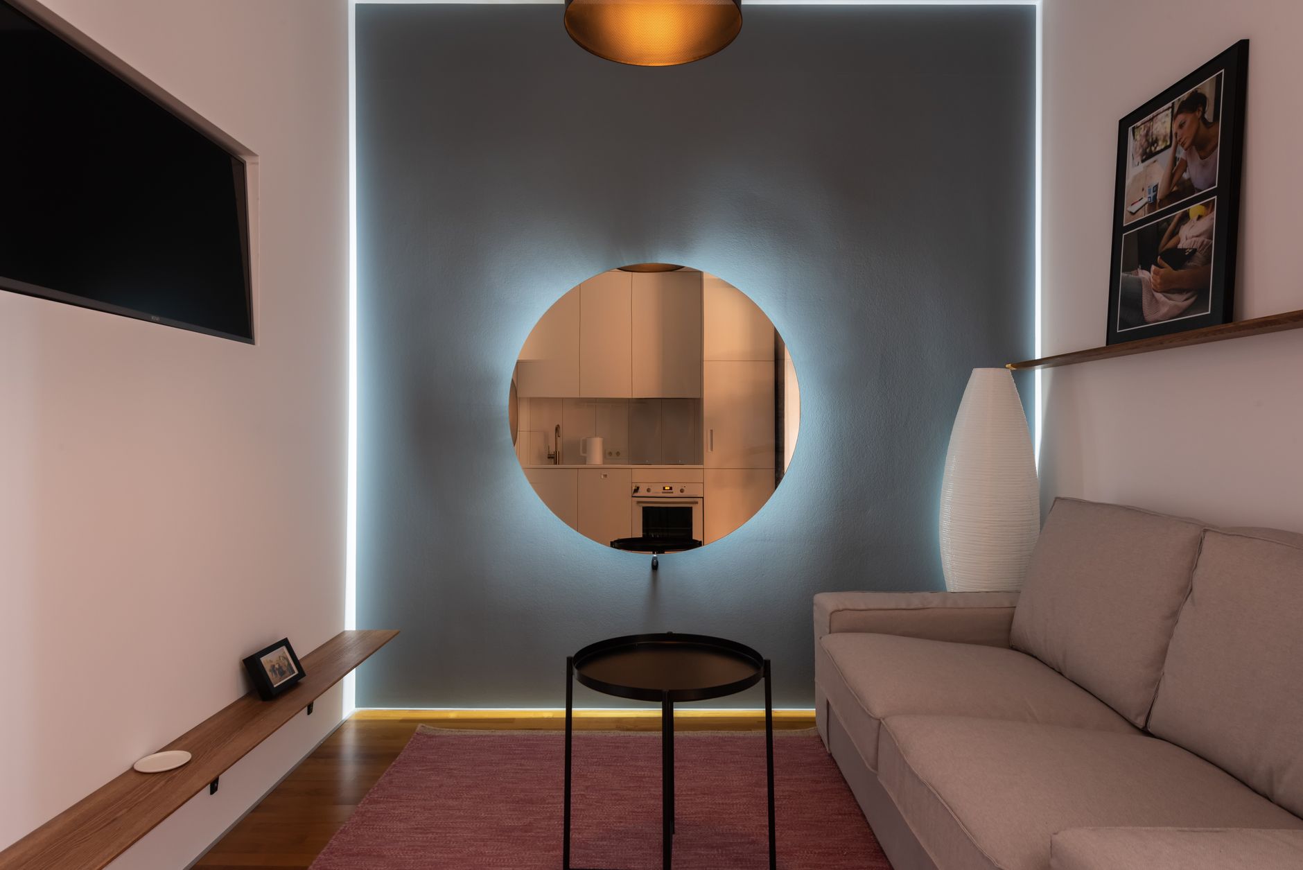 Contemporary lounge with frames and comfortable sofa in front of TV set near luminous wall with round mirror — Trójmiasto
