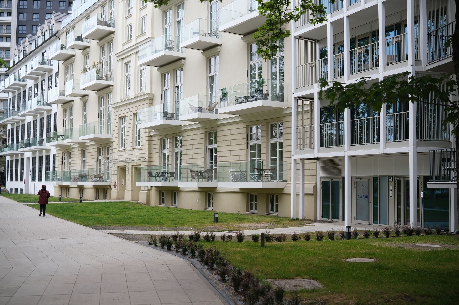 A modern apartment building with glass balconies and a pedestrian walking along the path. — Trójmiasto