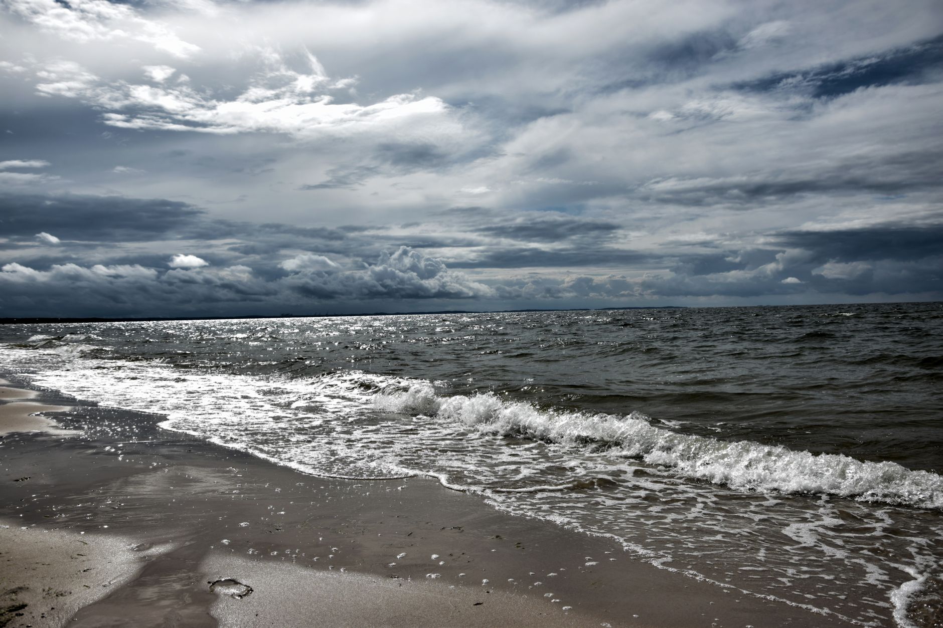 A dramatic view of a sandy beach with stormy clouds and waves crashing on the shore. — Trójmiasto