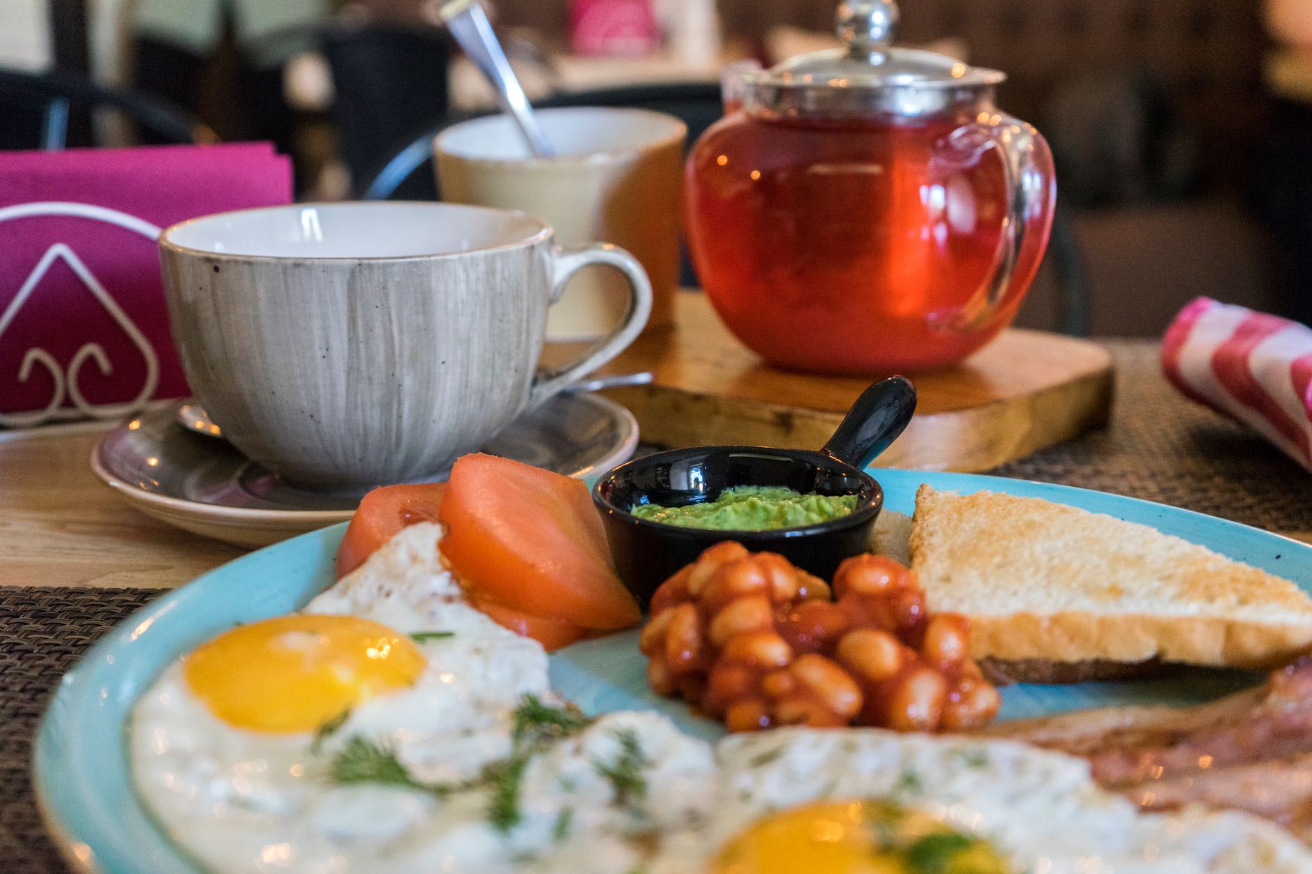 A close-up of a delicious hearty breakfast with eggs, bacon, beans, toast, and herbal tea. — Trójmiasto