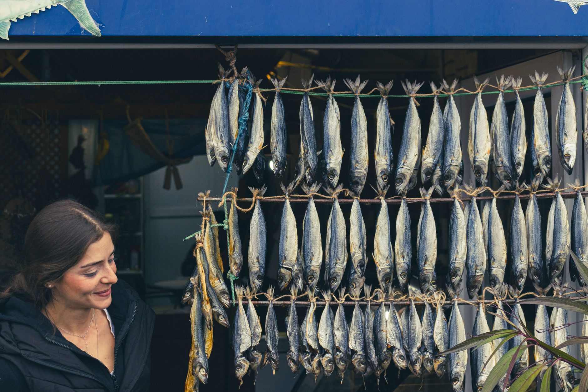 A woman smiles near a display of traditional dried fish at an outdoor market. — Trójmiasto