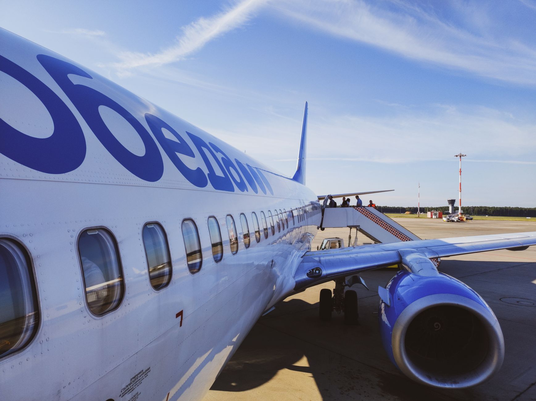 Side view of a commercial airplane with passengers boarding at a sunny airport. — Trójmiasto