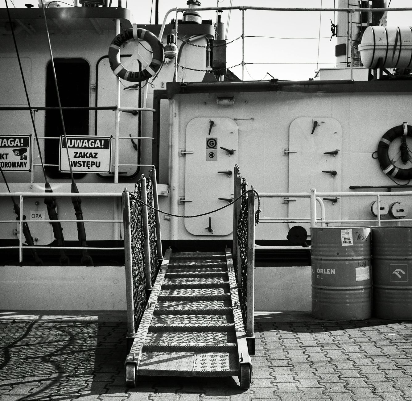 Black and white photo of a docked ship ladder in Gdańsk, Poland, featuring maritime safety signs. — Trójmiasto