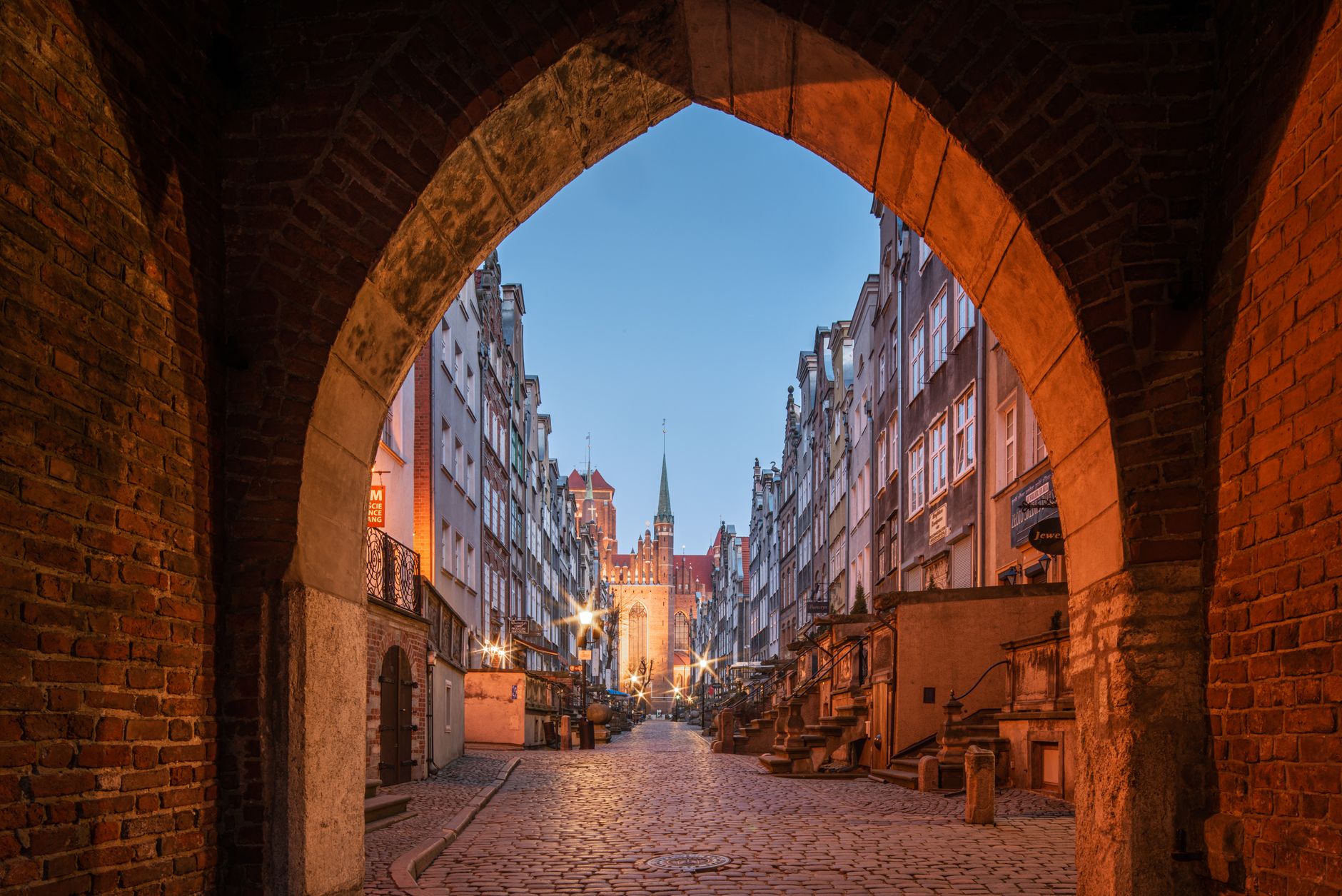 Explore a twilight view of a historic cobblestone street through an arch in Gdańsk's old town. — Trójmiasto