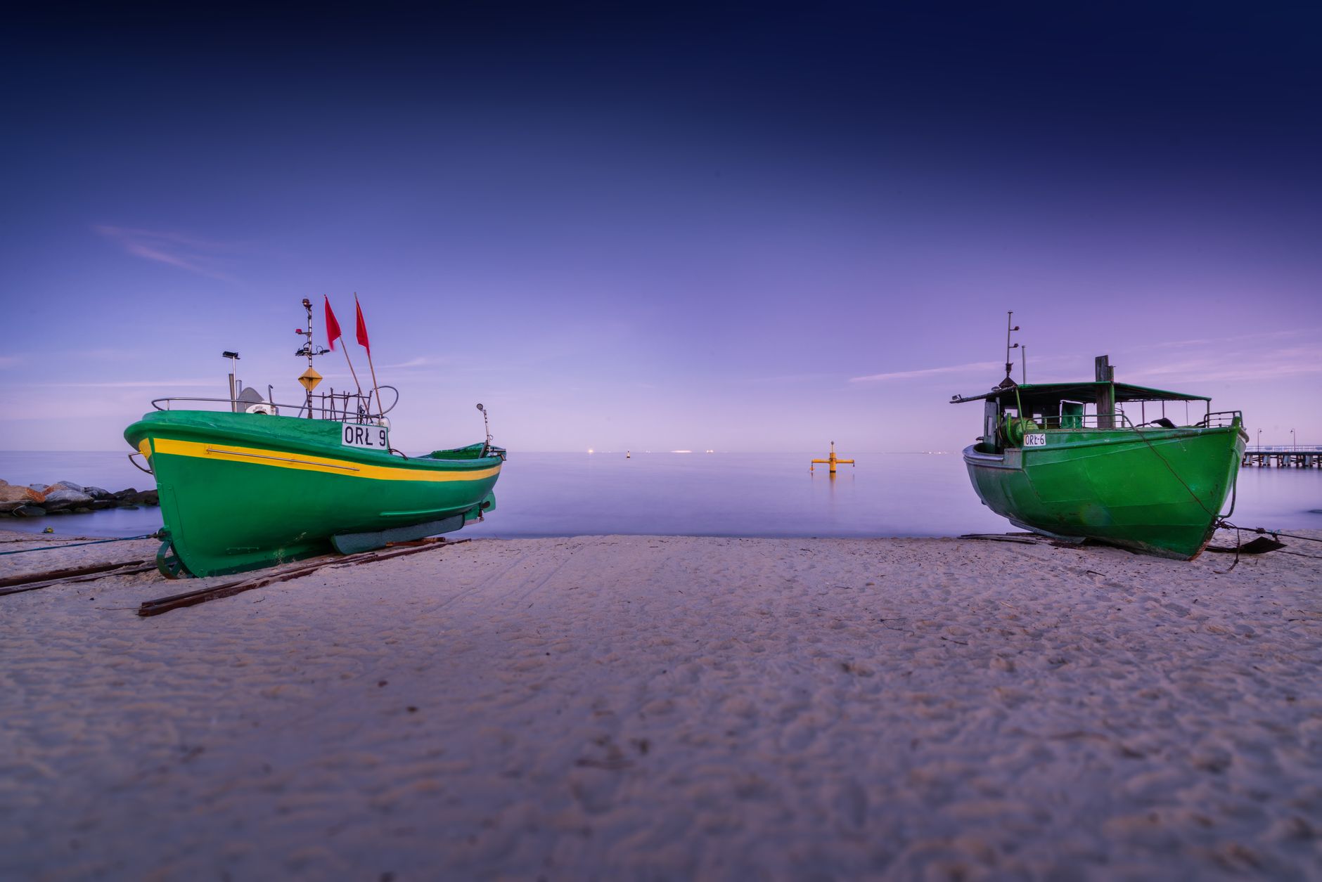 Small green boats located on empty sandy beach near calm sea under cloudless sky — Trójmiasto