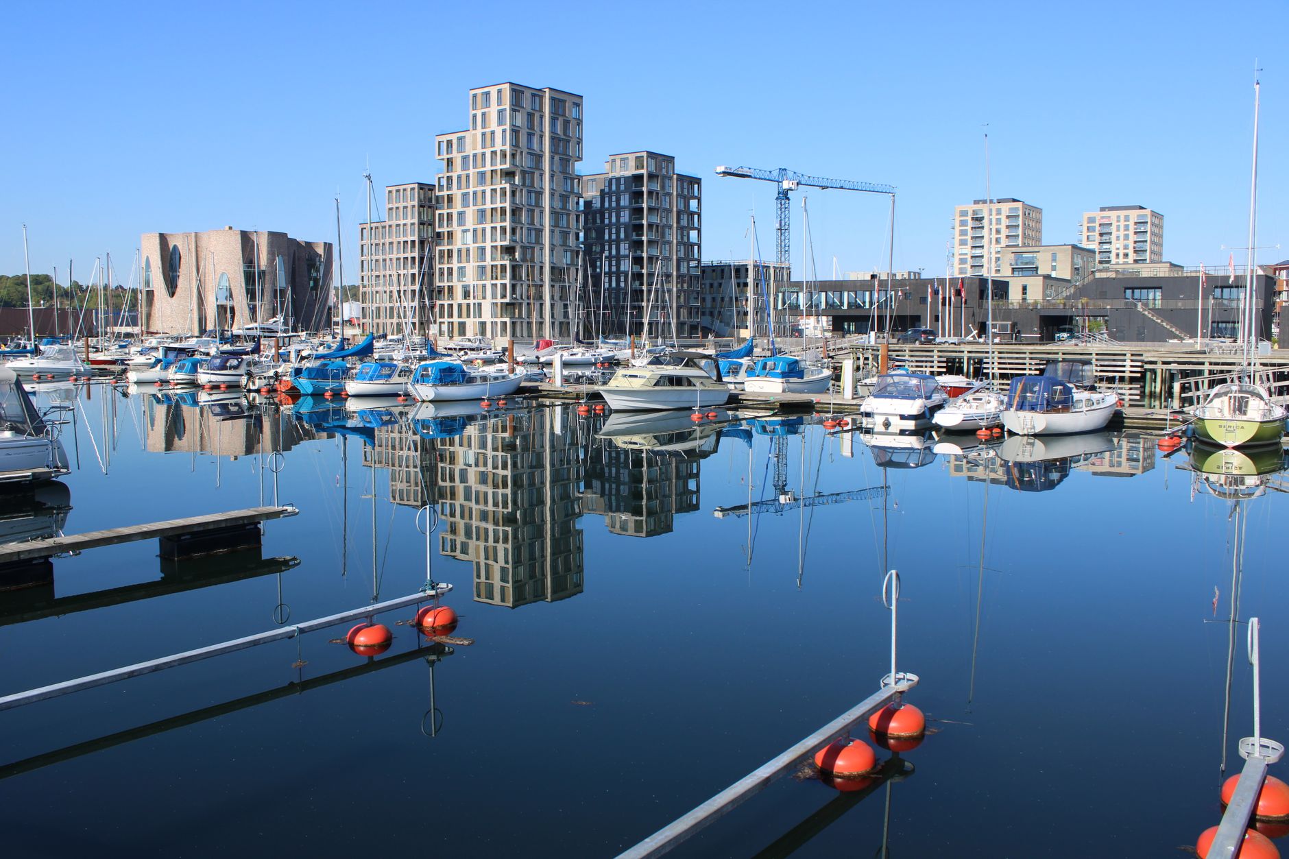Boats moored in Vejle's harbor, reflecting modern buildings under a clear sky. — Trójmiasto
