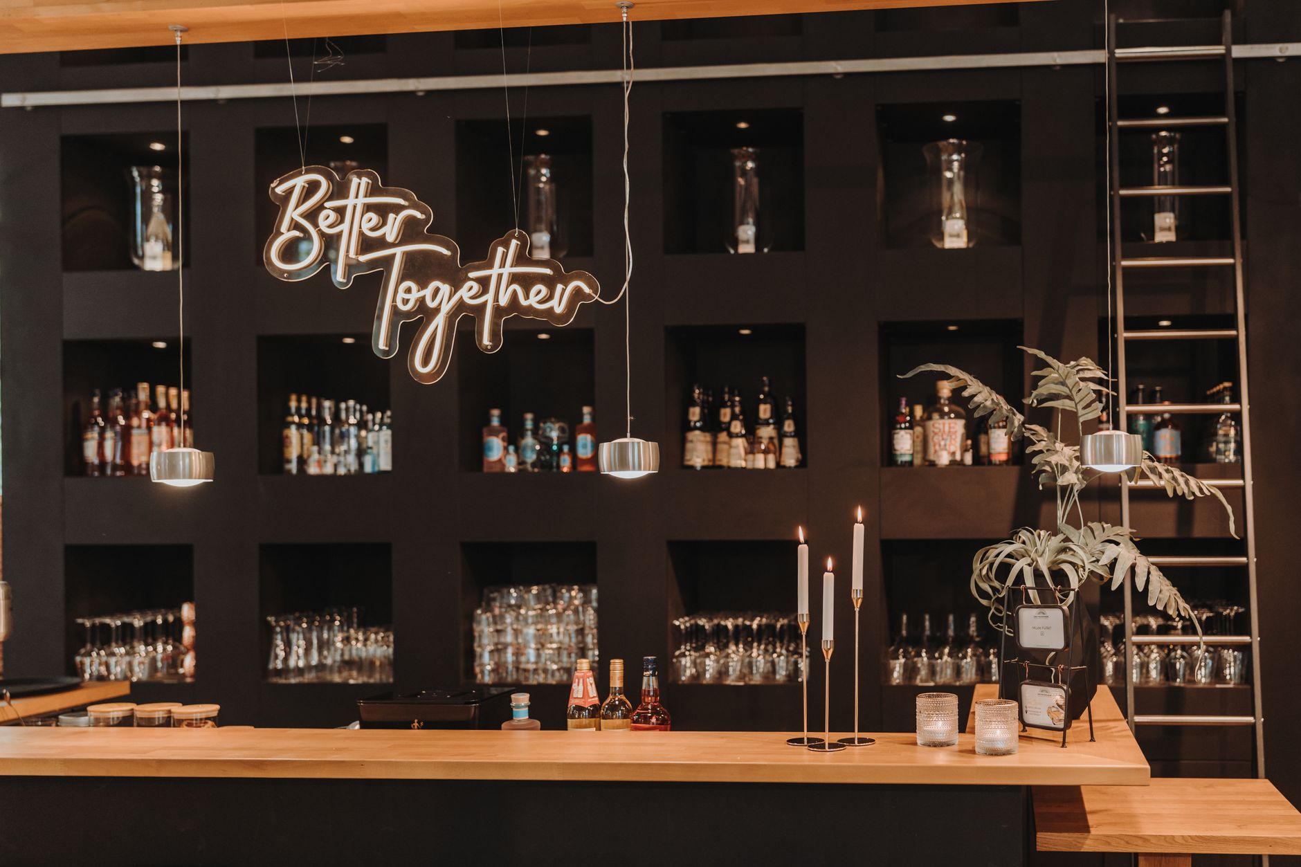 Stylish bar interior featuring a 'Better Together' sign, shelves of bottles, and glasses. — Trójmiasto