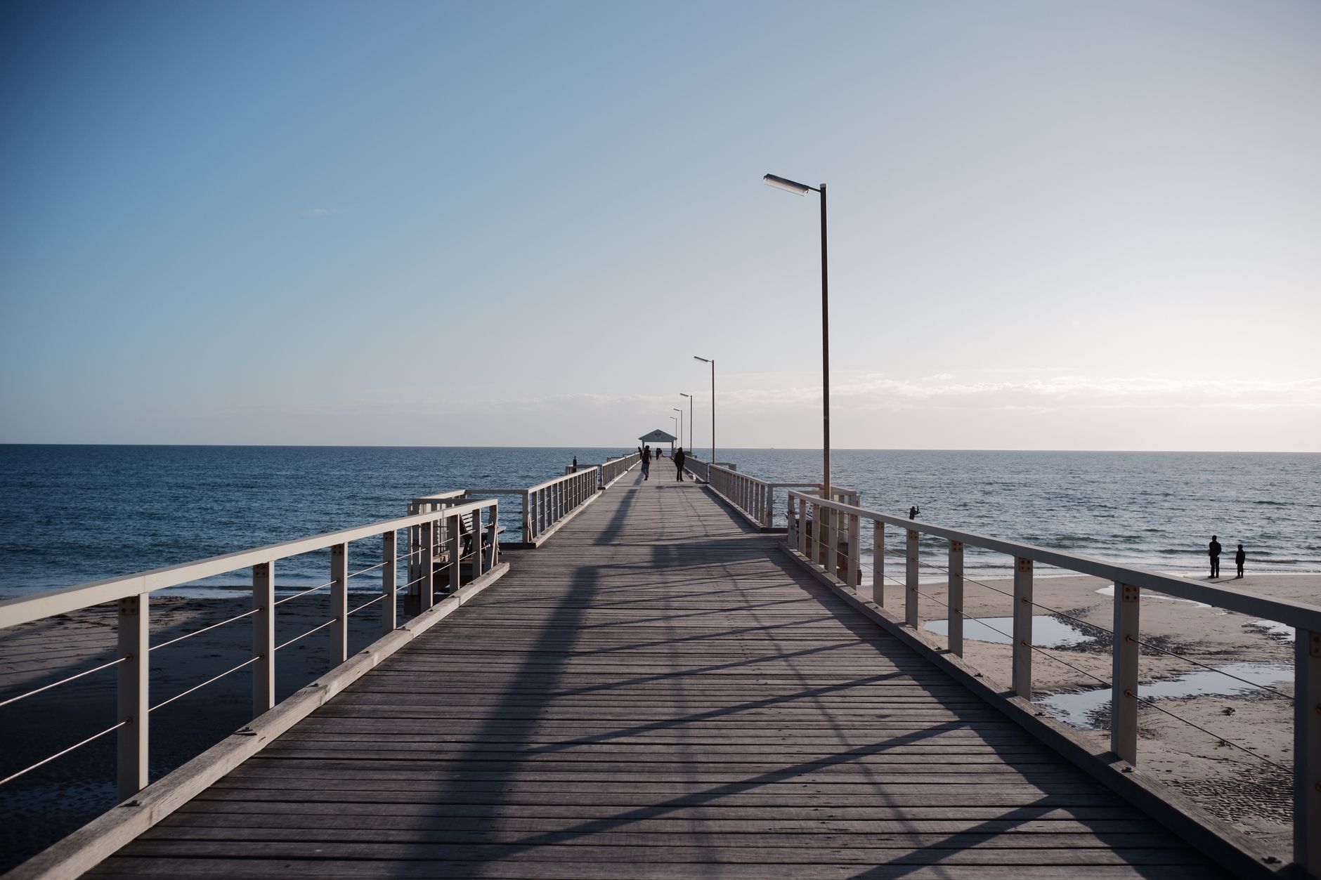 A wooden pier extends into the ocean under a clear sky, depicting a serene coastal scene. — Trójmiasto