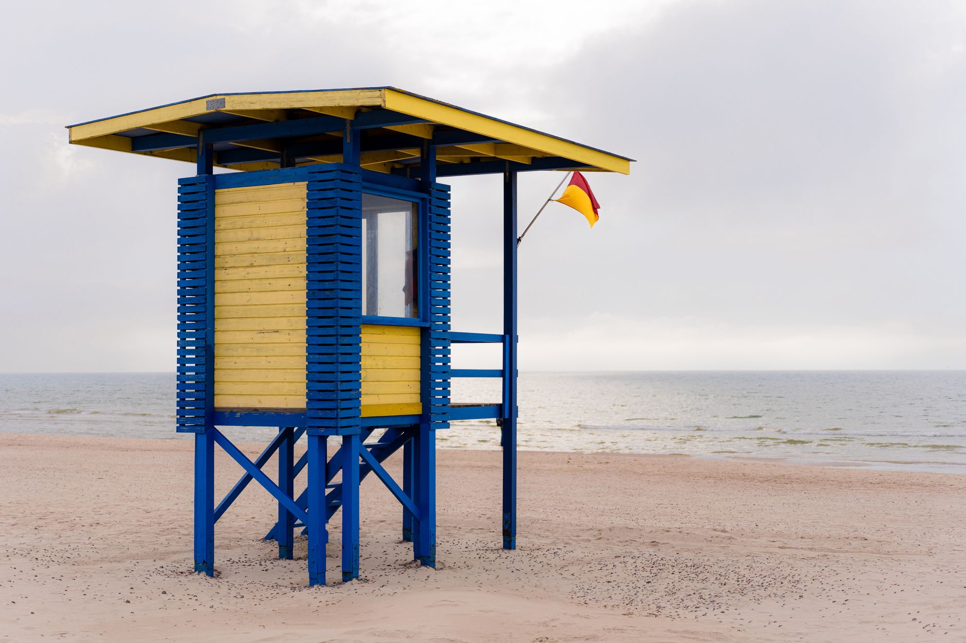 Bright yellow and blue lifeguard tower overlooking a calm sandy beach with a flag visible. — Trójmiasto