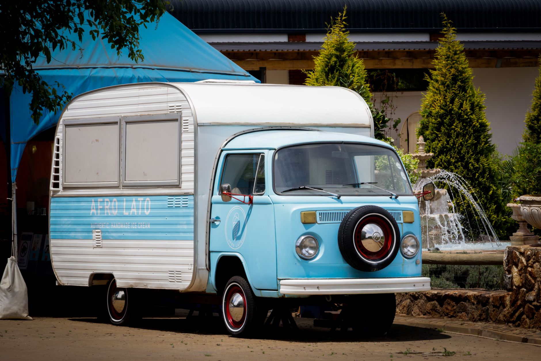 Charming vintage blue food truck with attached trailer parked outdoors near a fountain. — Trójmiasto