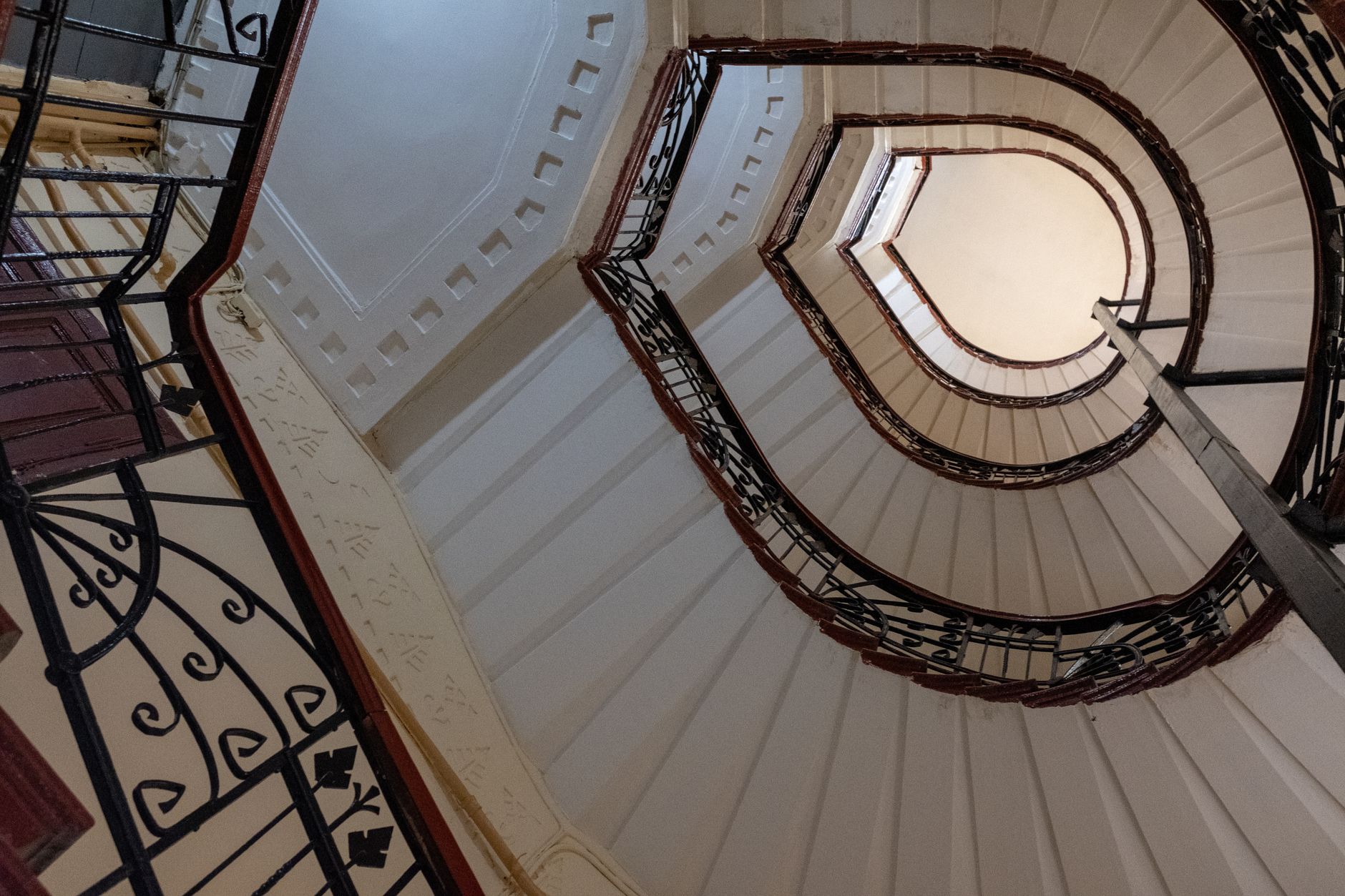 Upward view of a vintage curved staircase with intricate wrought iron railings in an indoor setting. — Trójmiasto