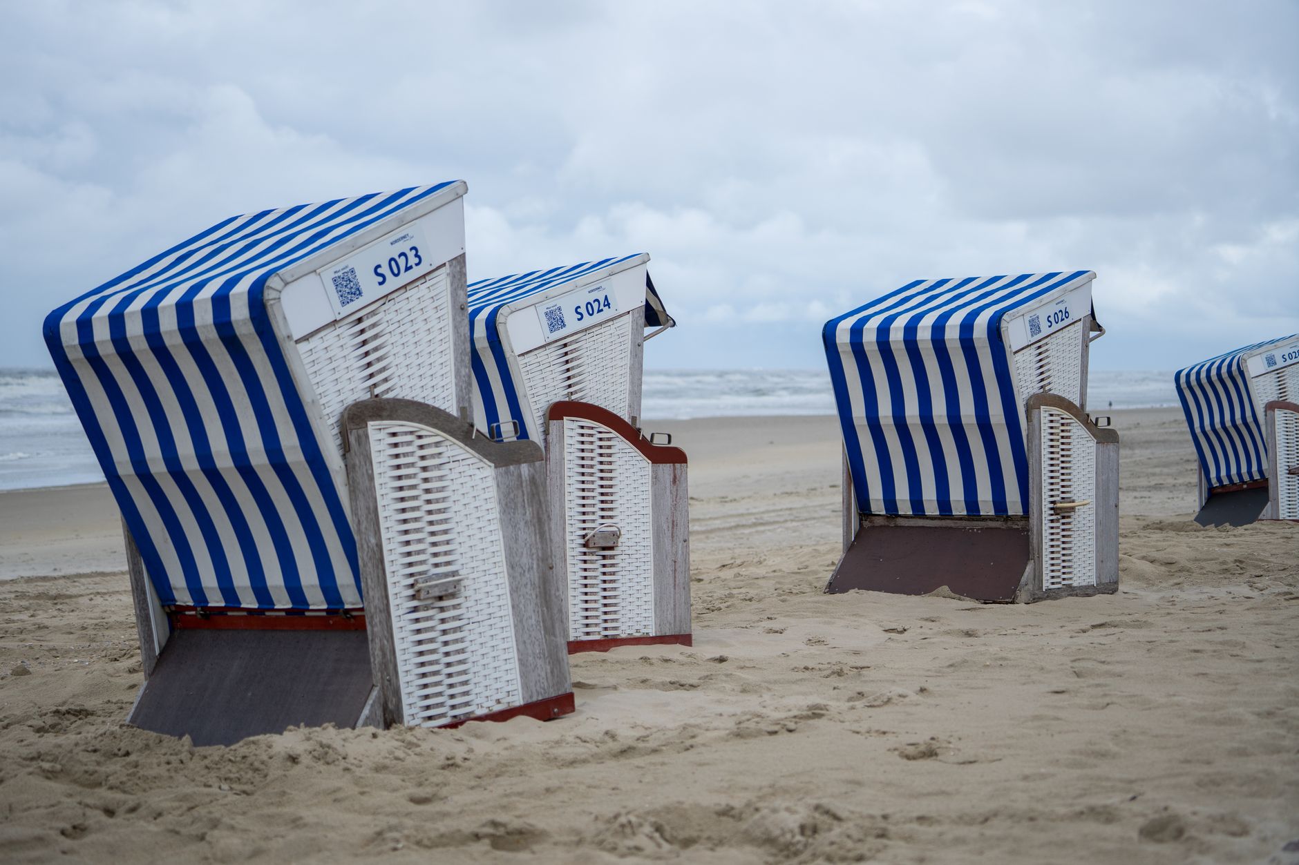 Charming beach scene with iconic blue and white striped Strandkorb chairs on a sandy shore. — Trójmiasto