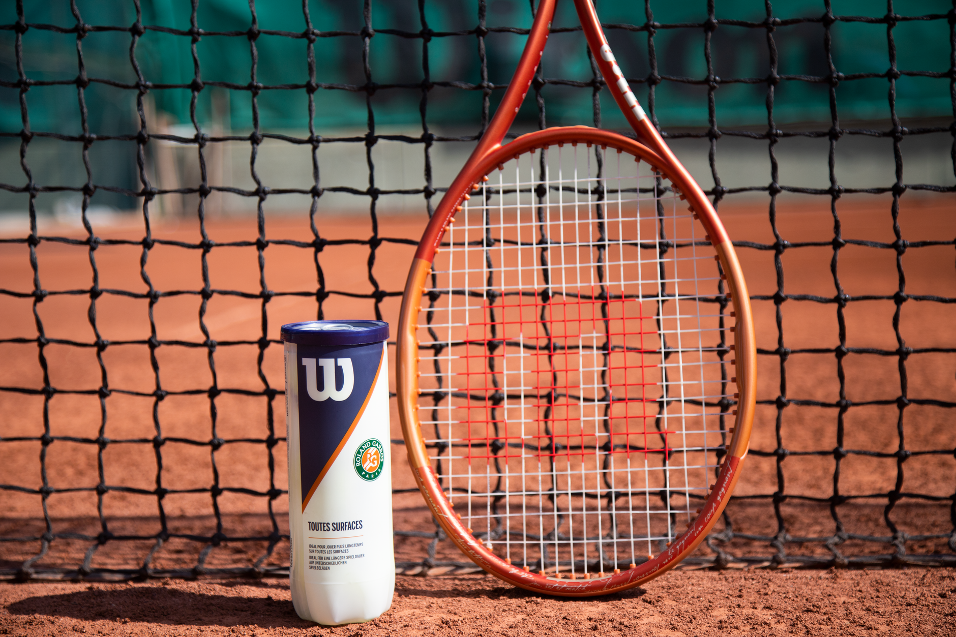 Tennis racket and ball can in front of a net on a clay court, showcasing sports equipment. — Trójmiasto
