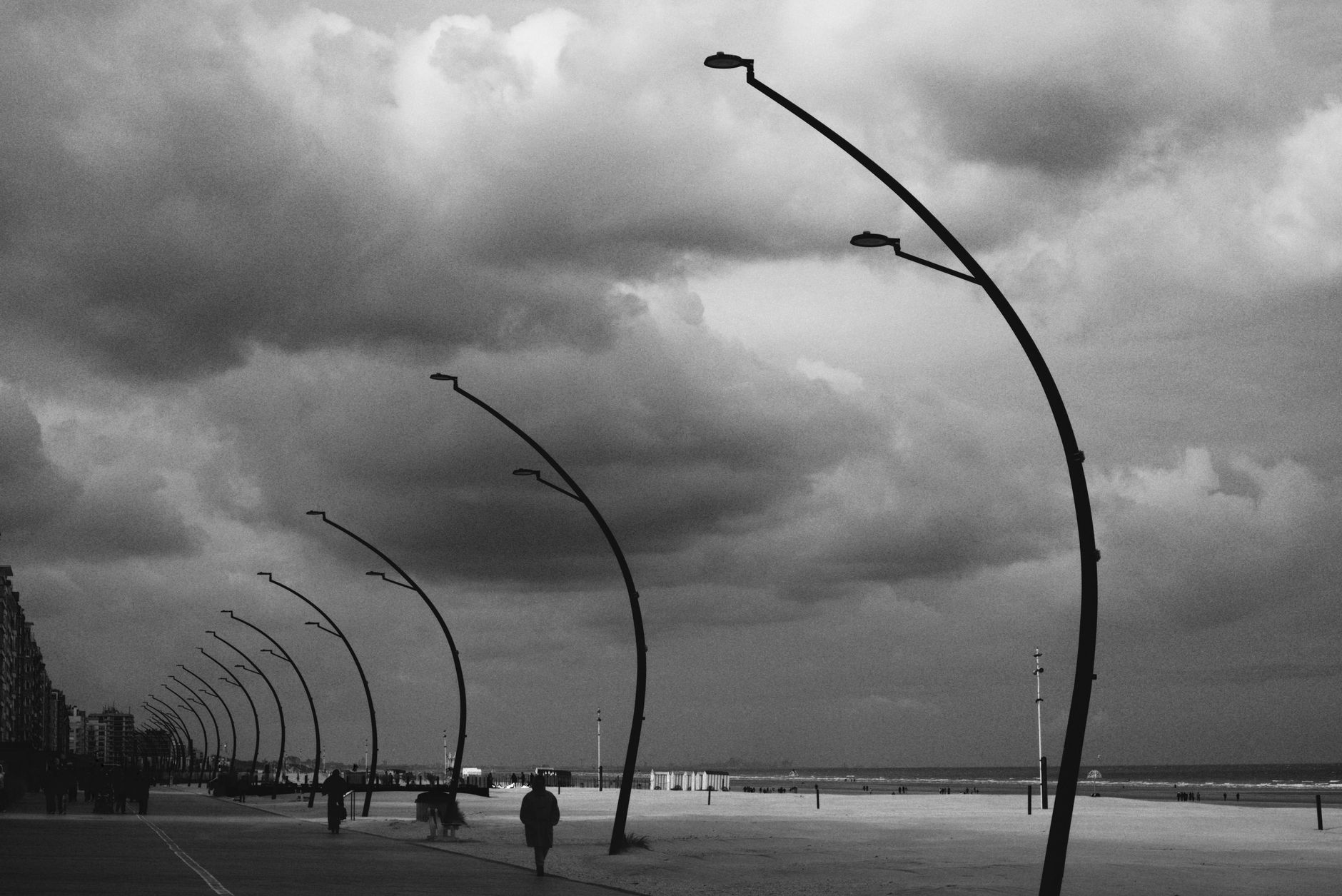 Monochrome view of a beach promenade with streetlamps under a cloudy sky. — Trójmiasto