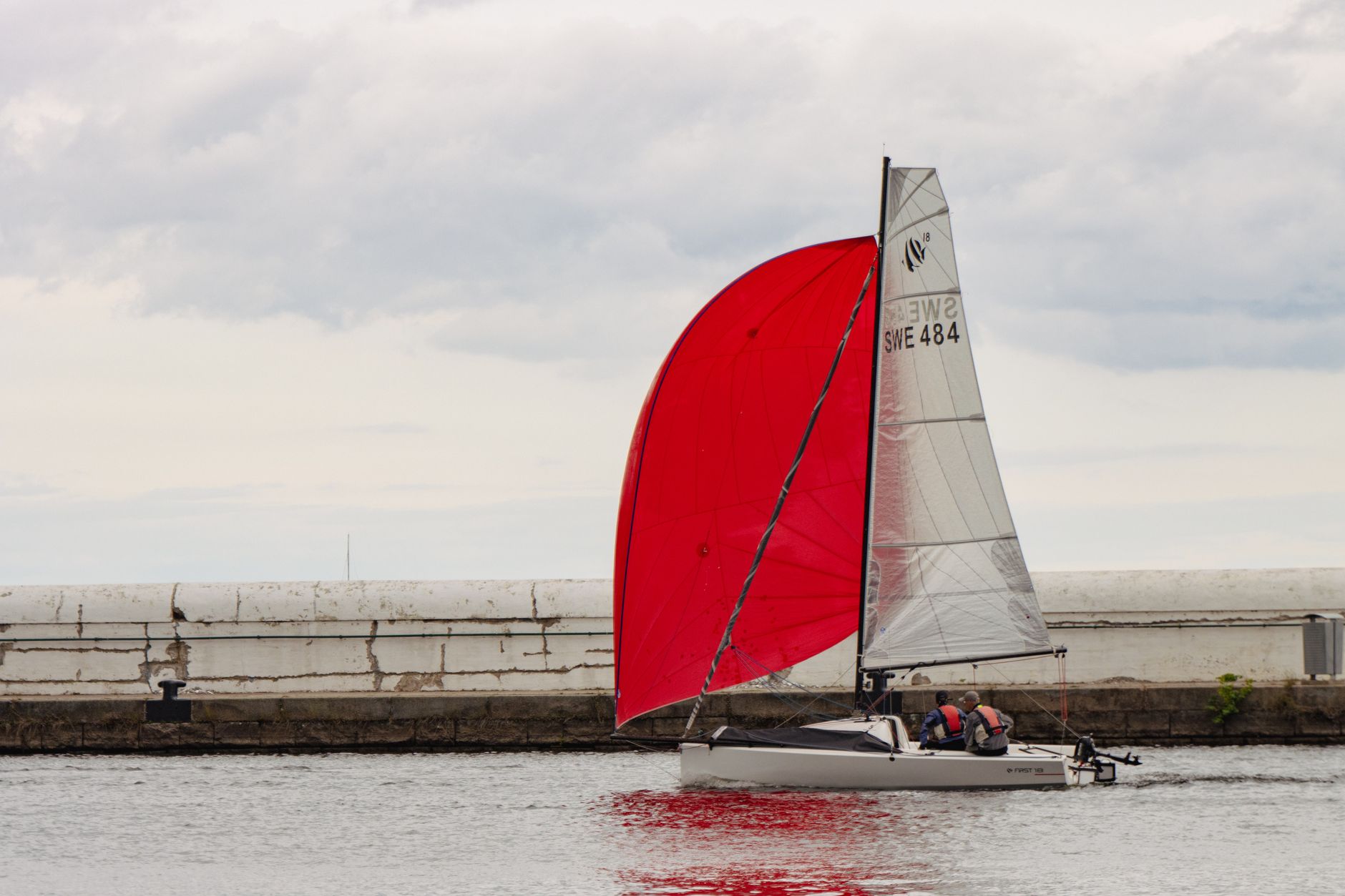 A sleek sailboat with a vibrant red sail glides across calm waters in Menton, France. — Trójmiasto