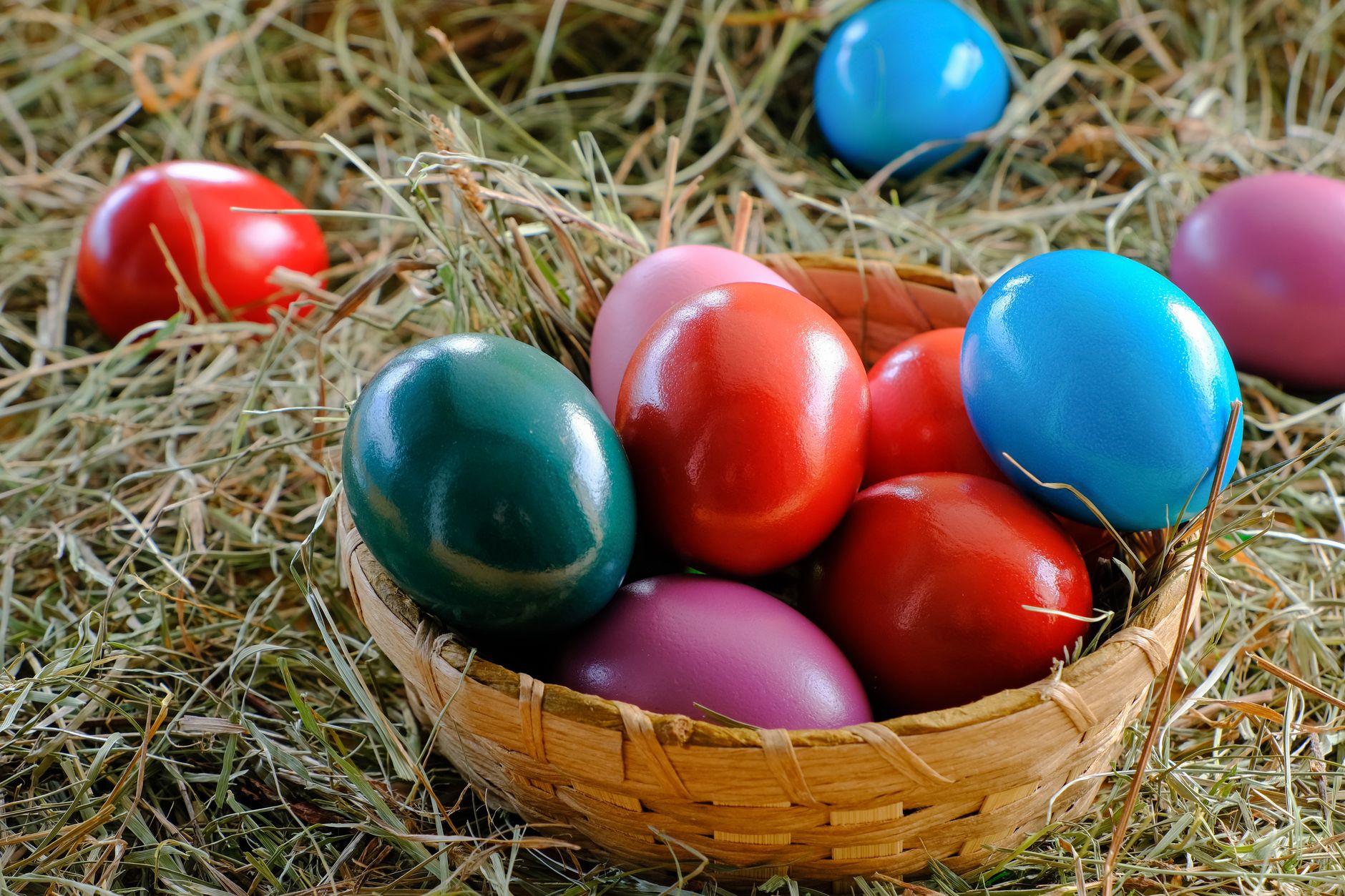 A vibrant display of colorful Easter eggs in a woven basket, set on a bed of hay. — Trójmiasto
