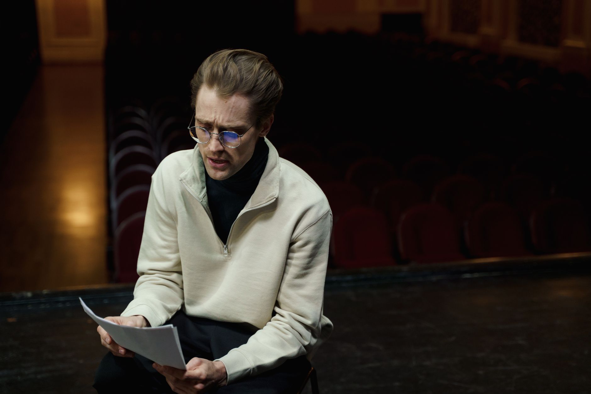 An actor rehearses lines on a theater stage, conveying focus and dedication in a dimly lit setting. — Trójmiasto