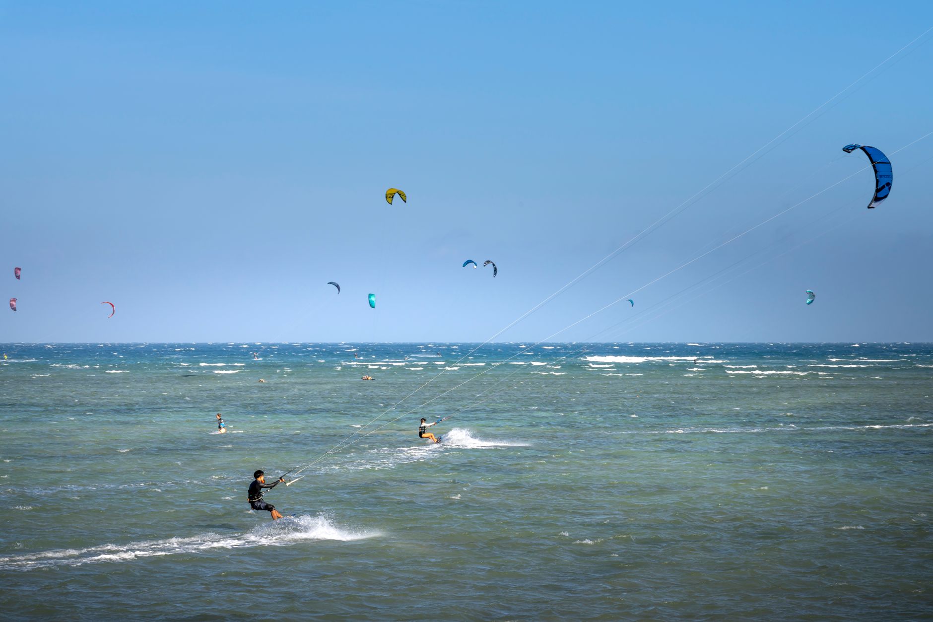Anonymous sportspeople with power kites practicing kitesurfing on wavy ocean under blue sky on stormy weather — Trójmiasto