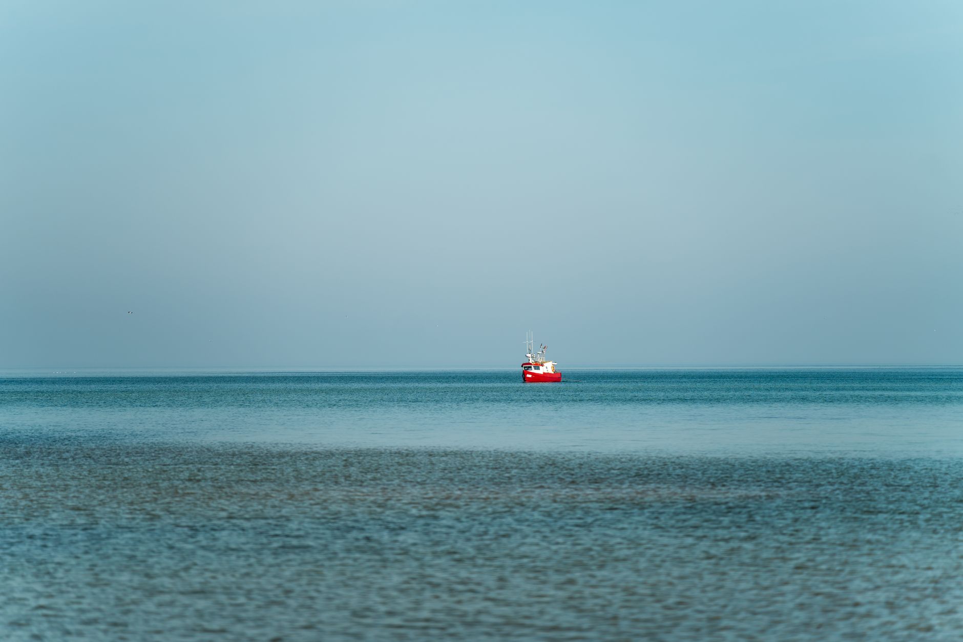 A lone red fishing boat floats on the serene waters of the Baltic Sea in Kołobrzeg, Poland. — Trójmiasto