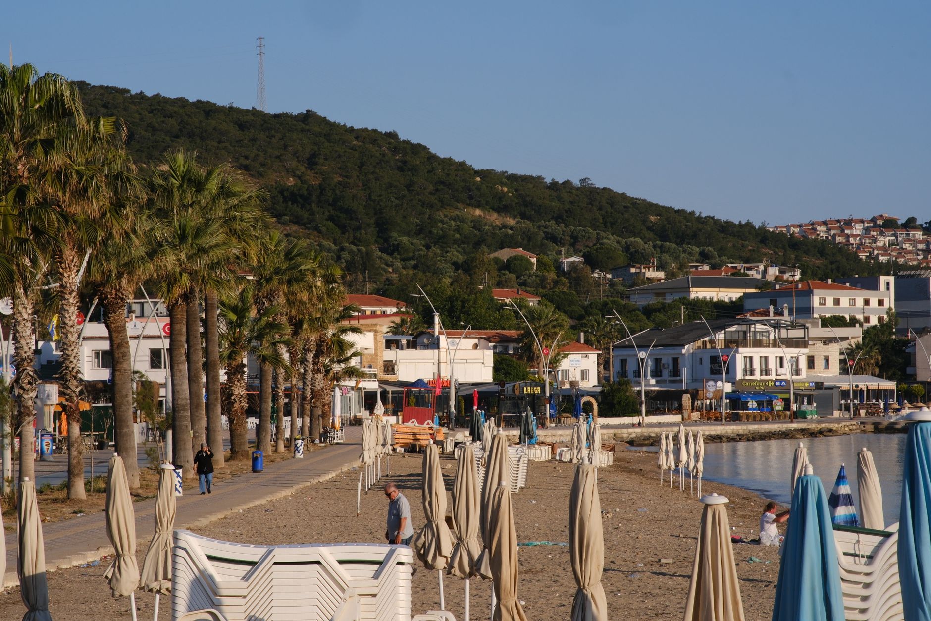 Scenic view of the beachfront promenade in Foça, İzmir, Türkiye with palm trees and umbrellas. — Trójmiasto