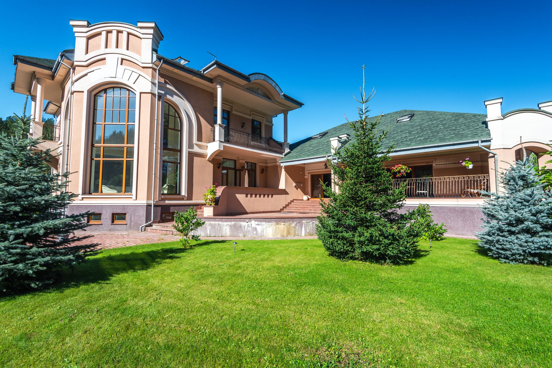 Modern luxury villa with large windows, surrounded by lush green lawn and trees. — Trójmiasto