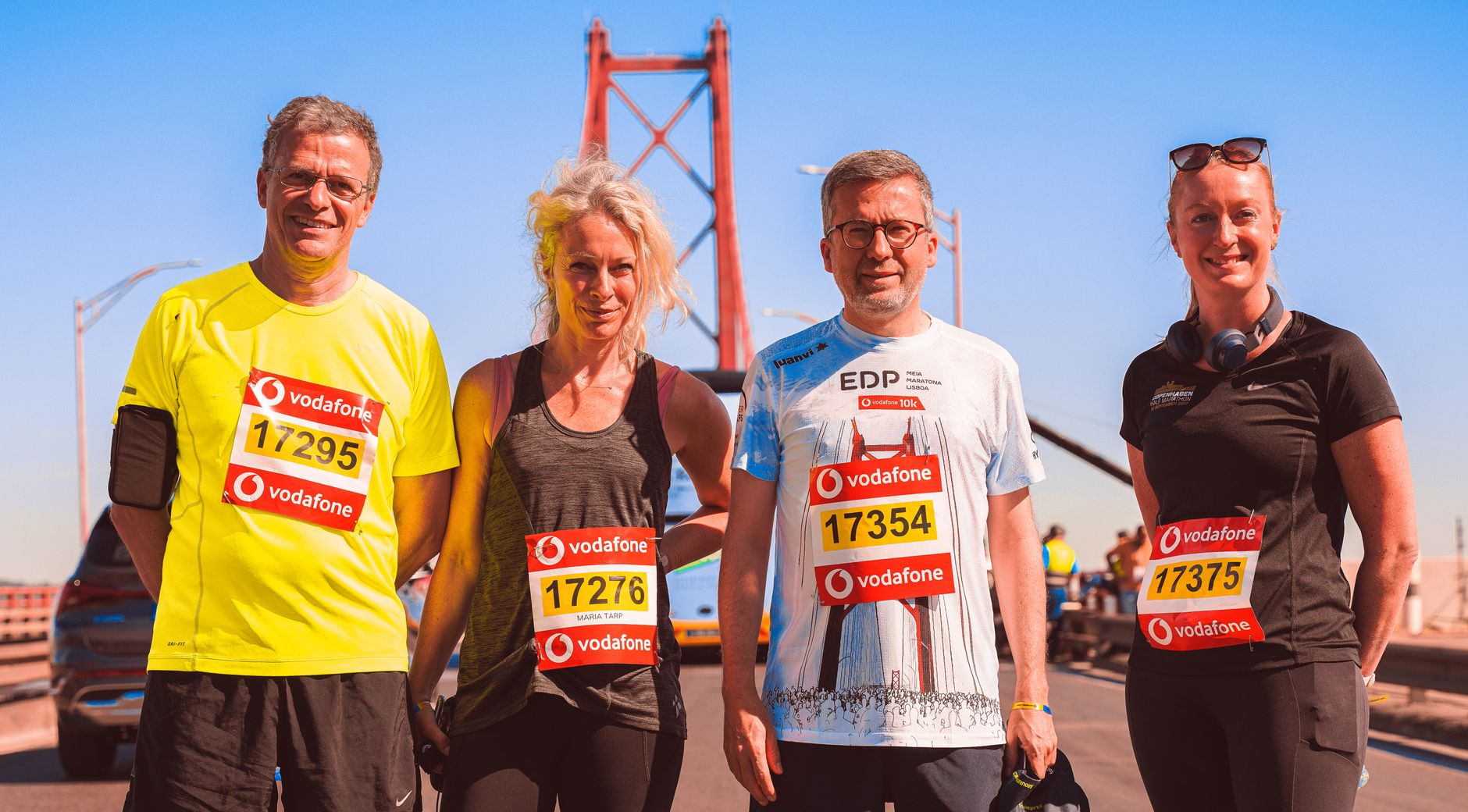 Four marathon runners smiling on a sunny day with a bridge in the background. — Trójmiasto
