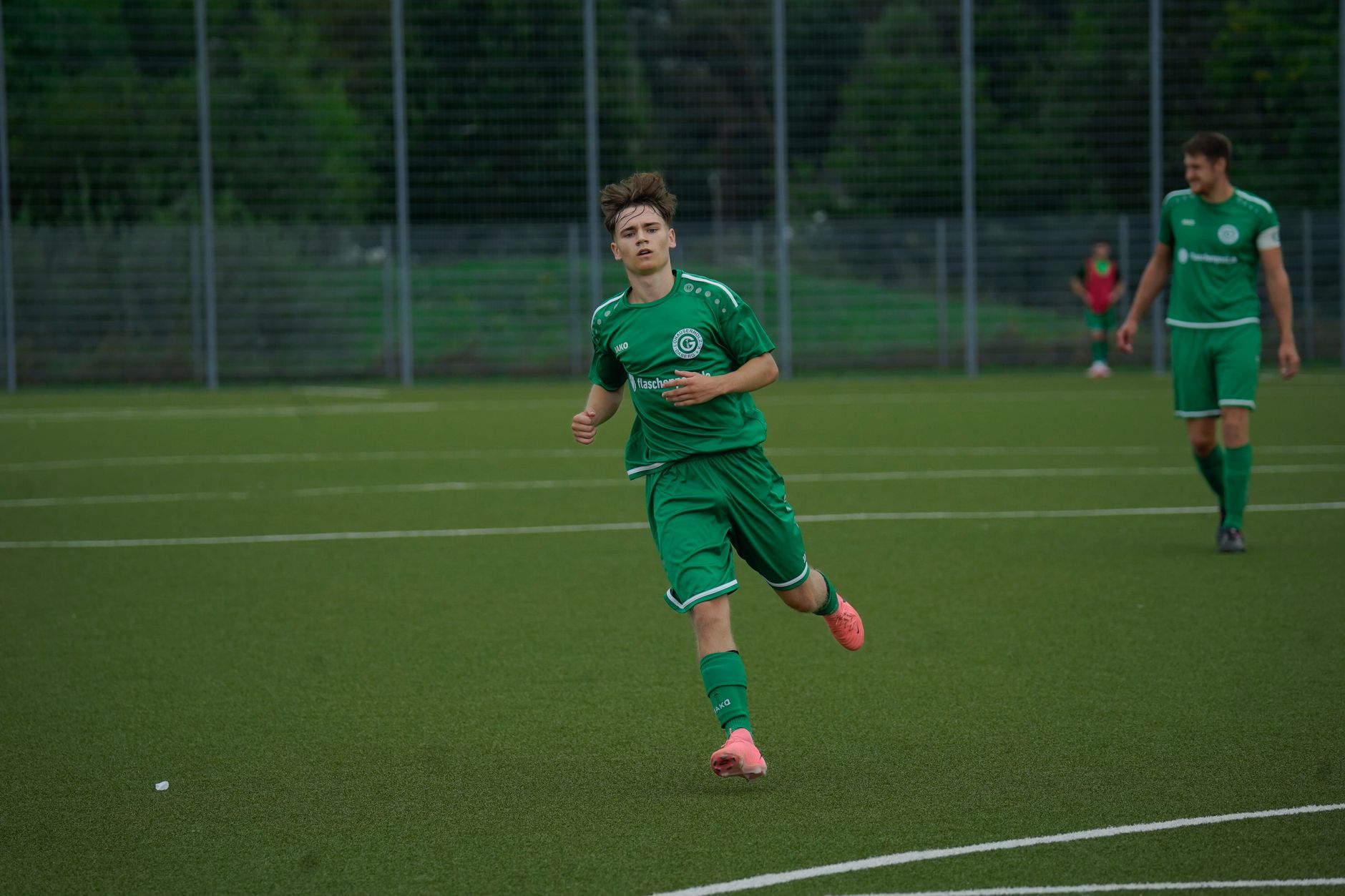 A football player in a green jersey running during an outdoor match on a grass pitch. — Trójmiasto