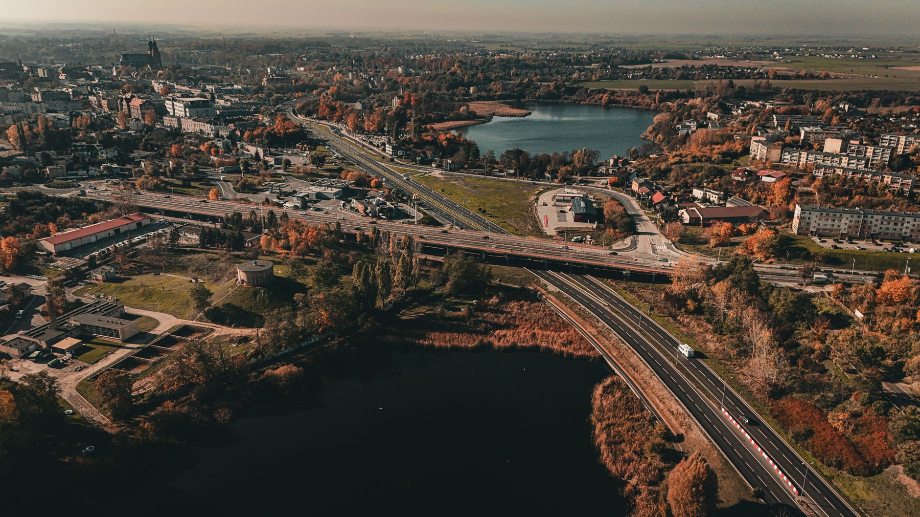 Aerial view capturing an autumn urban landscape with roads, buildings, and lakes. — Trójmiasto